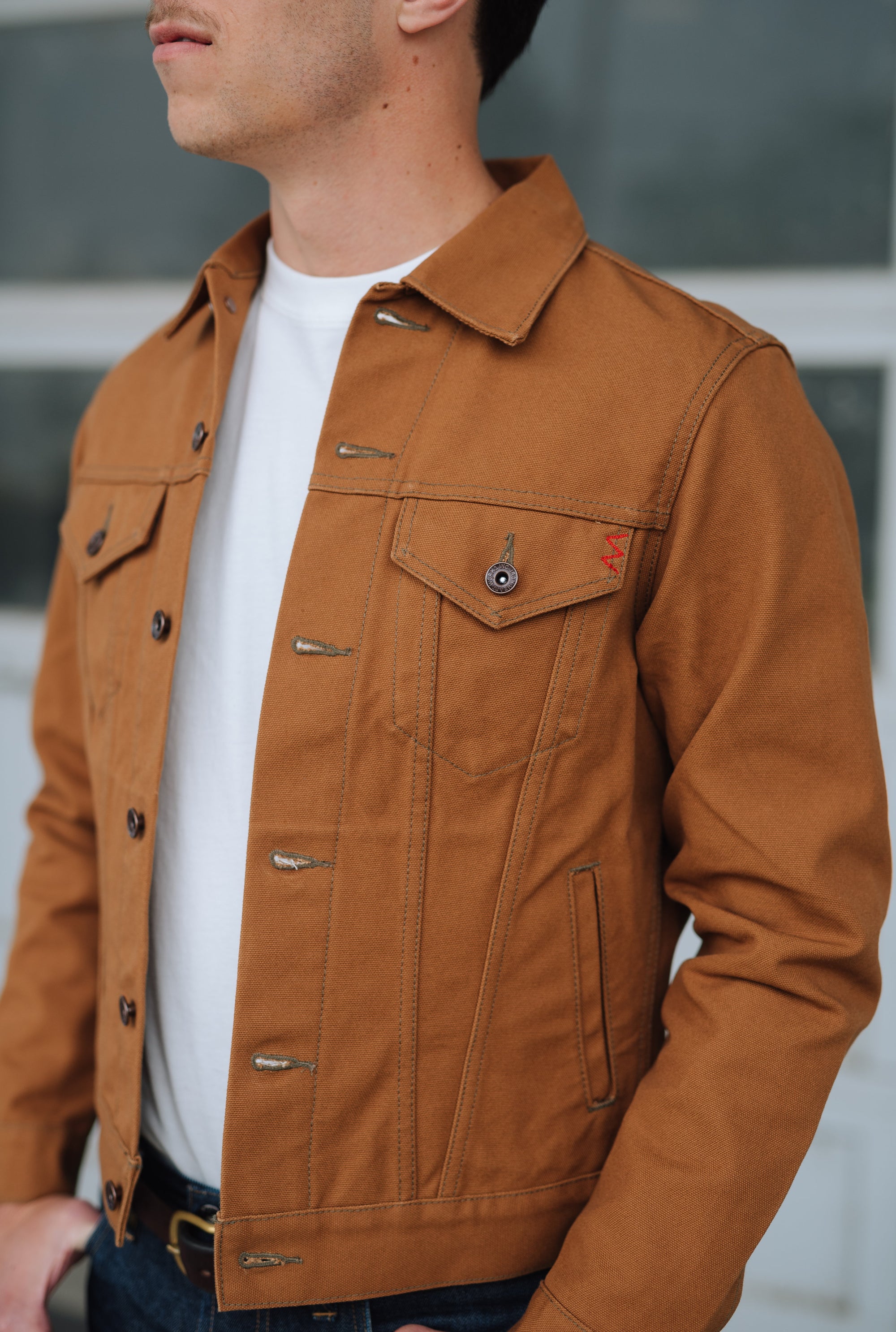 Close-up of man wearing Iron Heart Type III duck canvas brown jacket over white shirt with button details