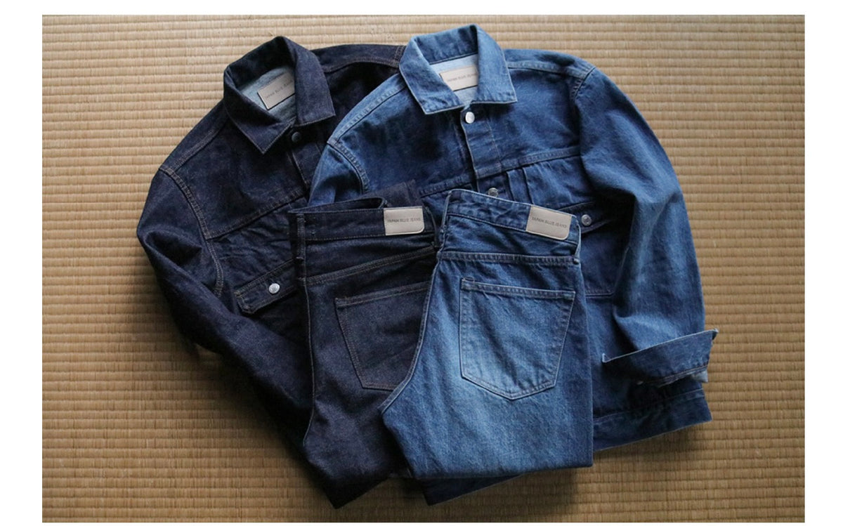 Two sets of dark and light blue denim jackets and jeans laid on a textured mat, casual apparel