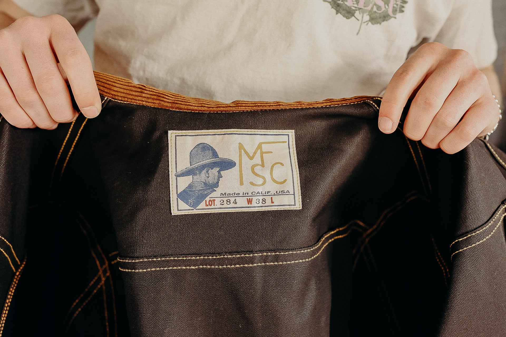 Hands holding open dark fabric with a Mister Freedom label featuring a man in a hat and size details W38 L on durable jacket