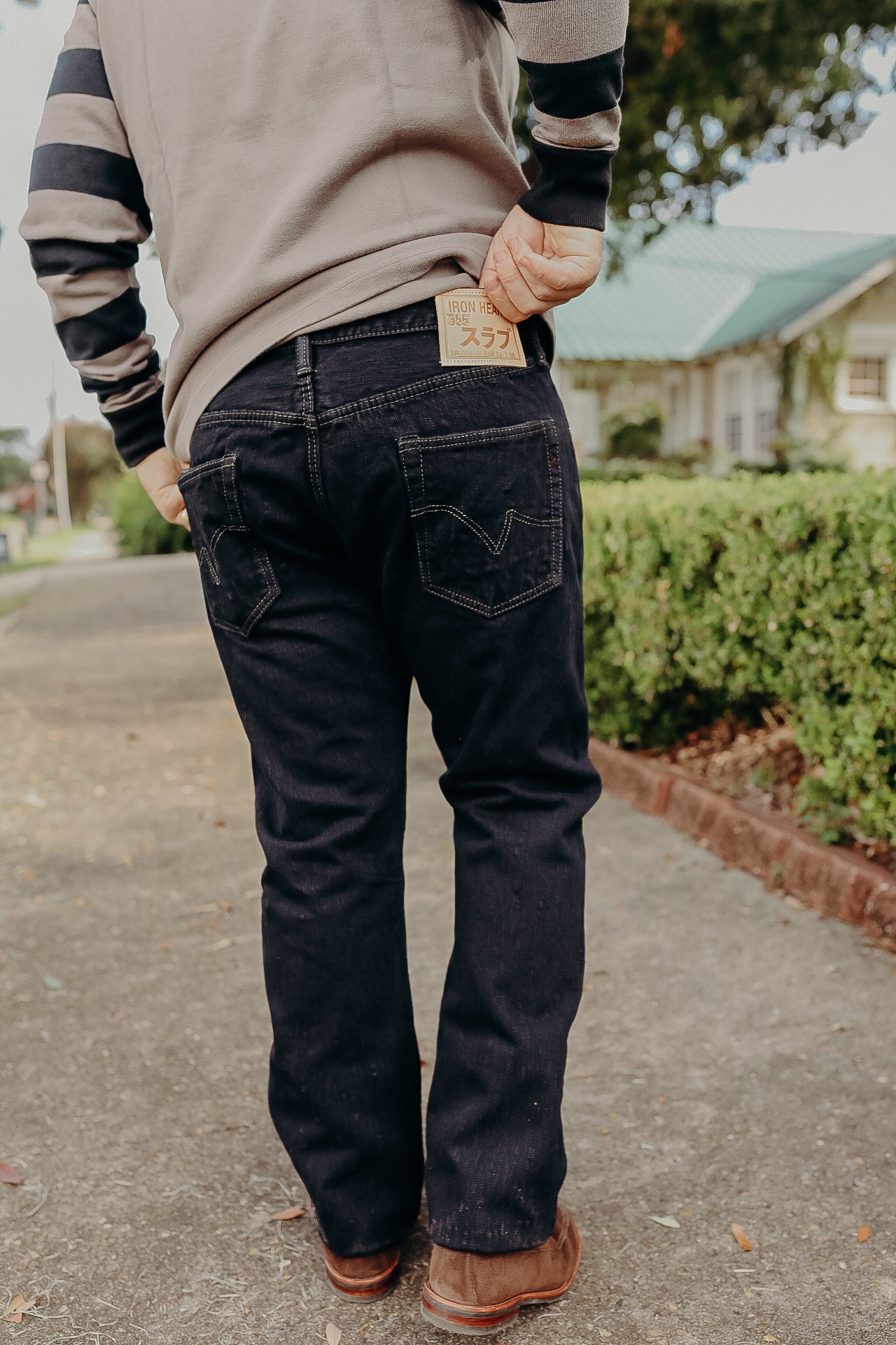Person wearing dark denim jeans with Iron Heart label on back pocket, standing outdoors on sidewalk