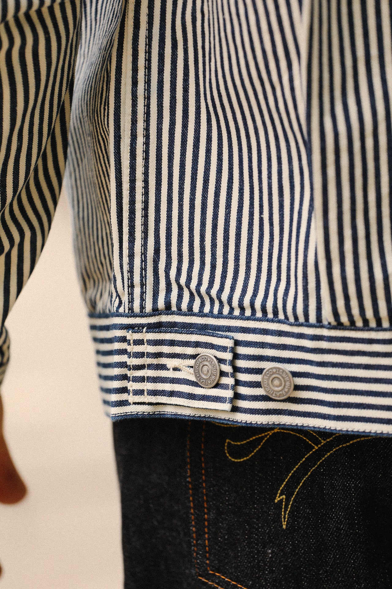 Close-up of navy and white hickory stripe jacket cuff with silver snap buttons and visible stitching