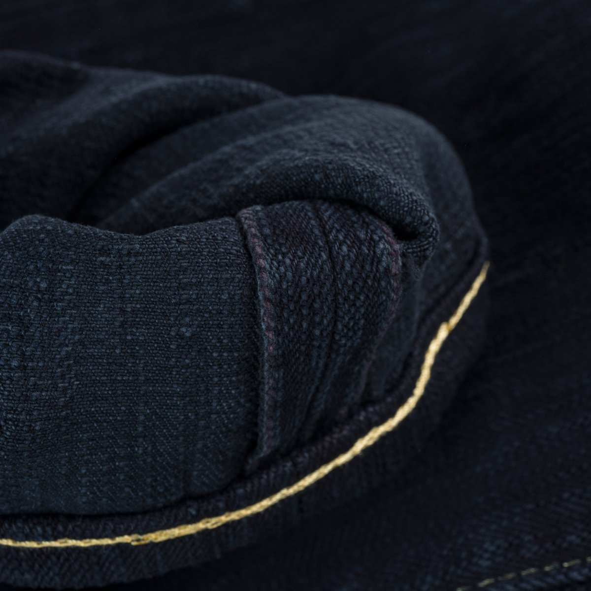 Close-up of dark denim fabric with rolled cuff and yellow stitching detail from Iron Shop Provisions