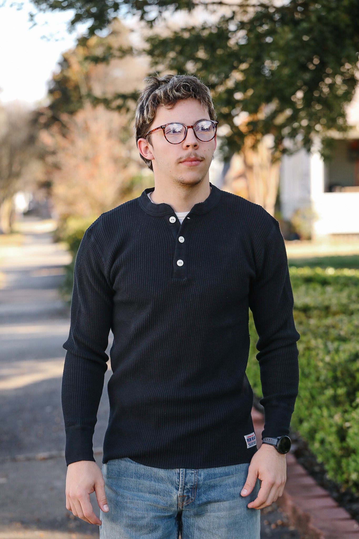 Man wearing a black long-sleeve shirt and glasses standing outdoors.