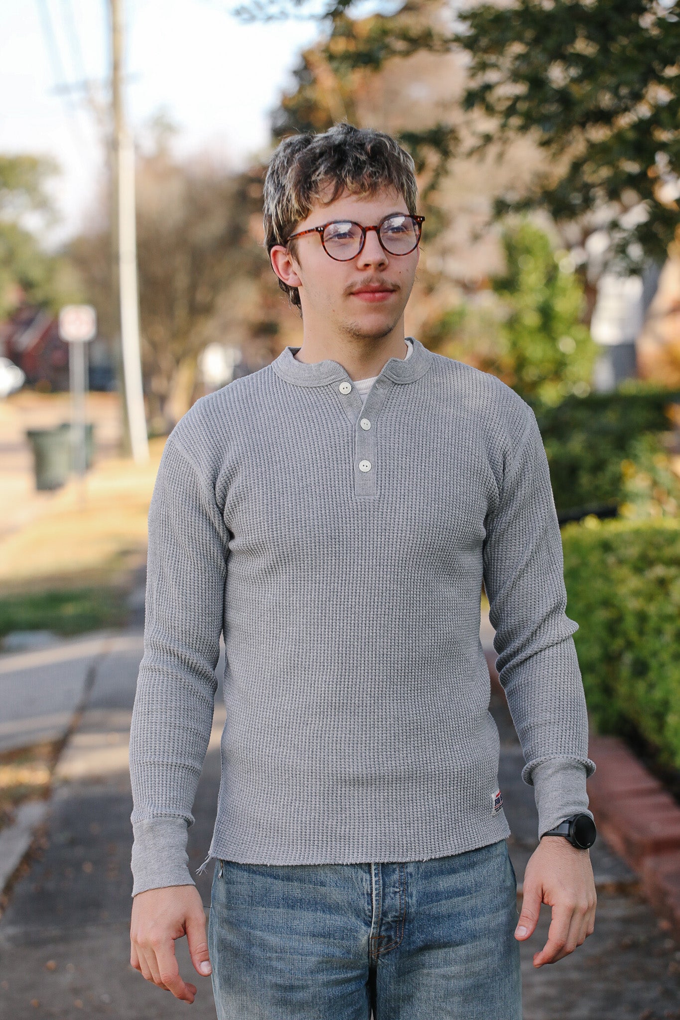 Man wearing a gray long-sleeve shirt and jeans standing outdoors.