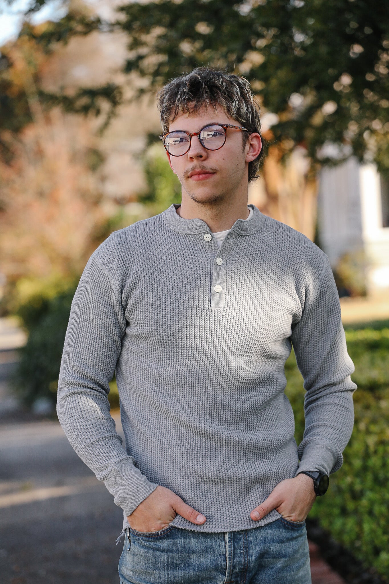 Person wearing a gray long-sleeve shirt and glasses outdoors