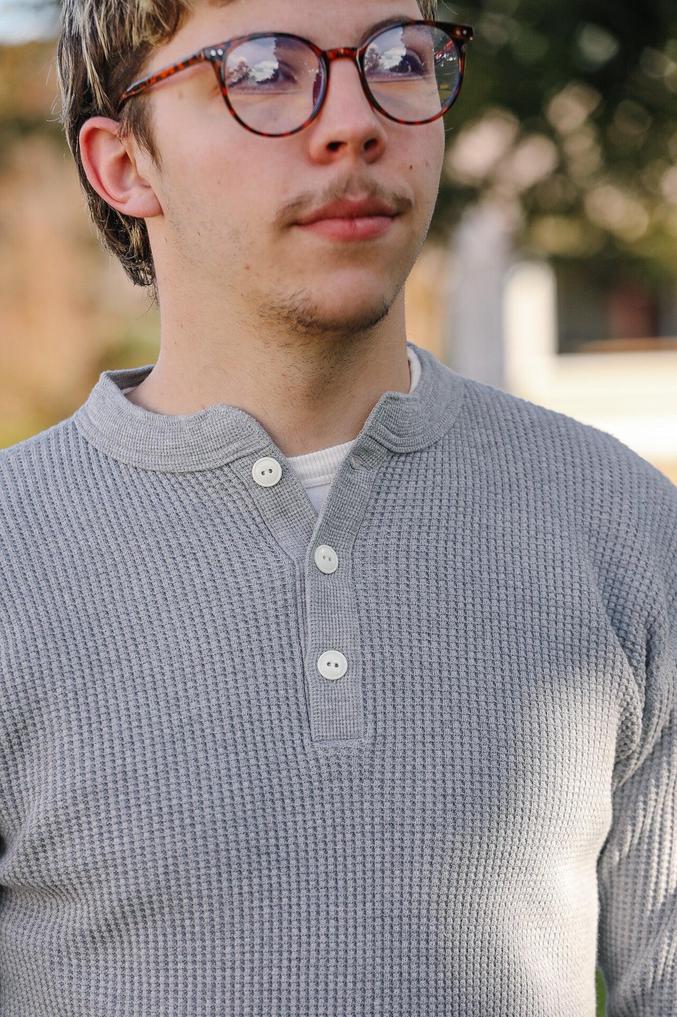 Person wearing a gray long-sleeve shirt with a blurred outdoor background