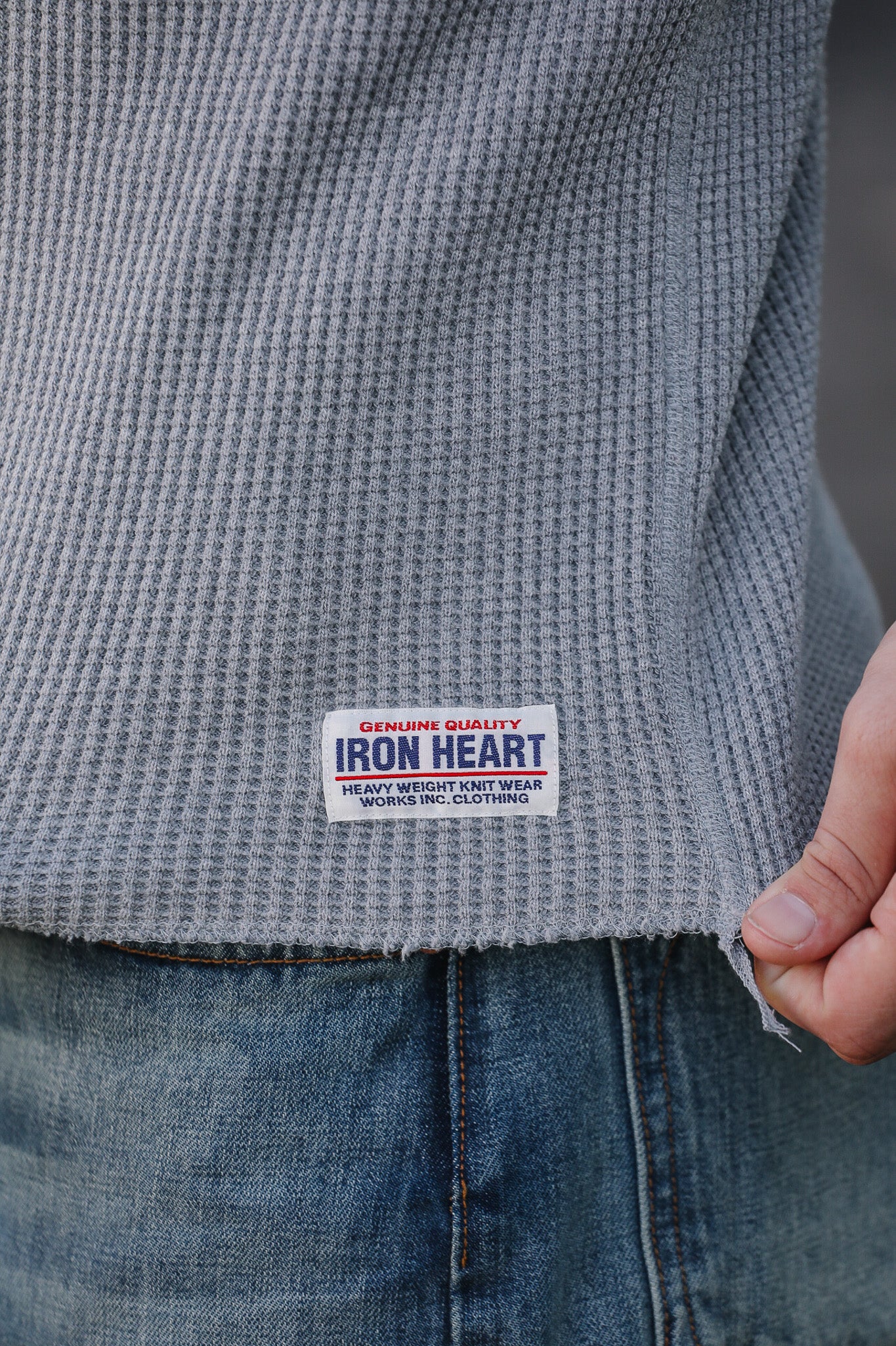 Gray textured sweater with Iron Heart label held by a hand