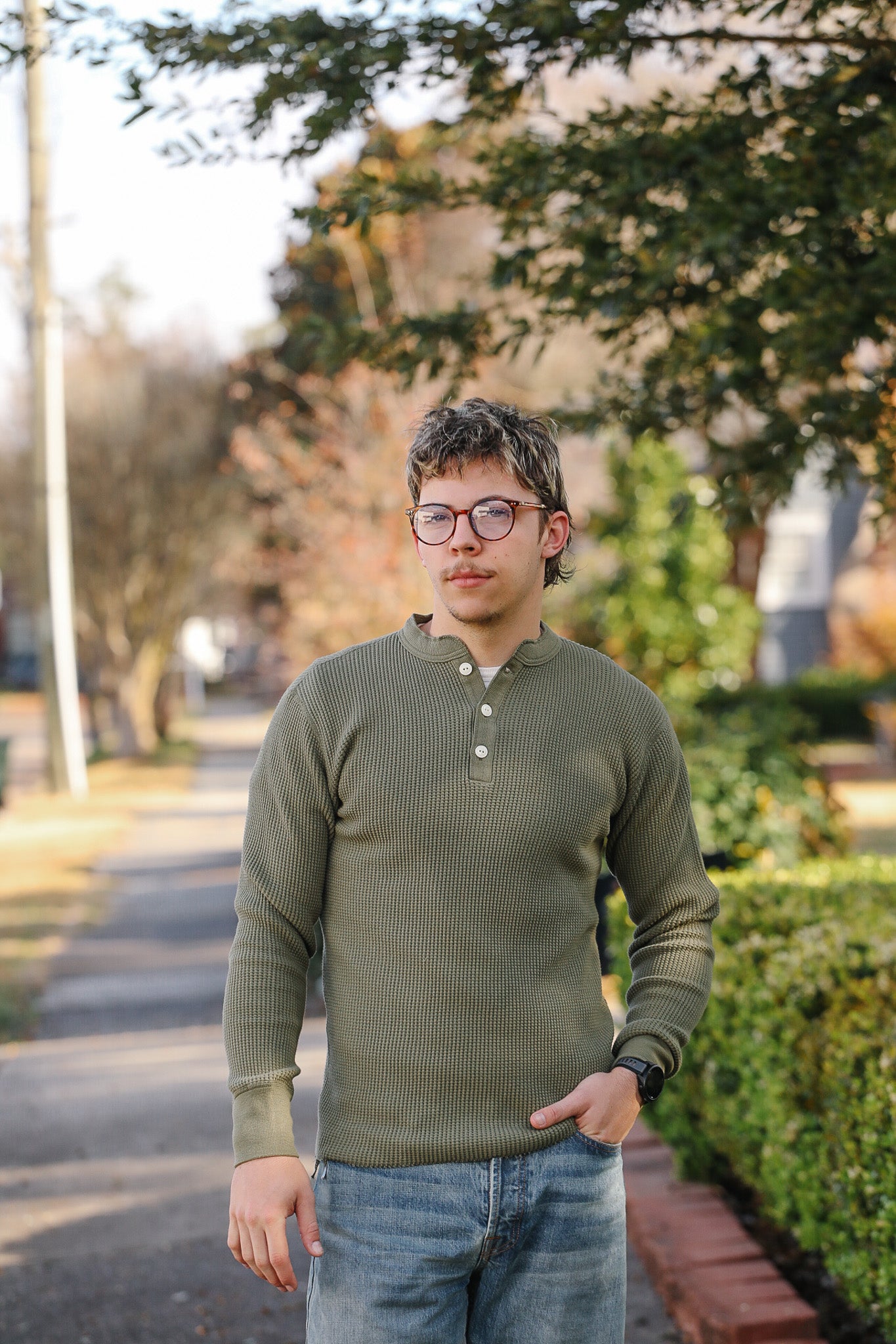 Person wearing a green long-sleeve shirt and glasses standing outdoors.