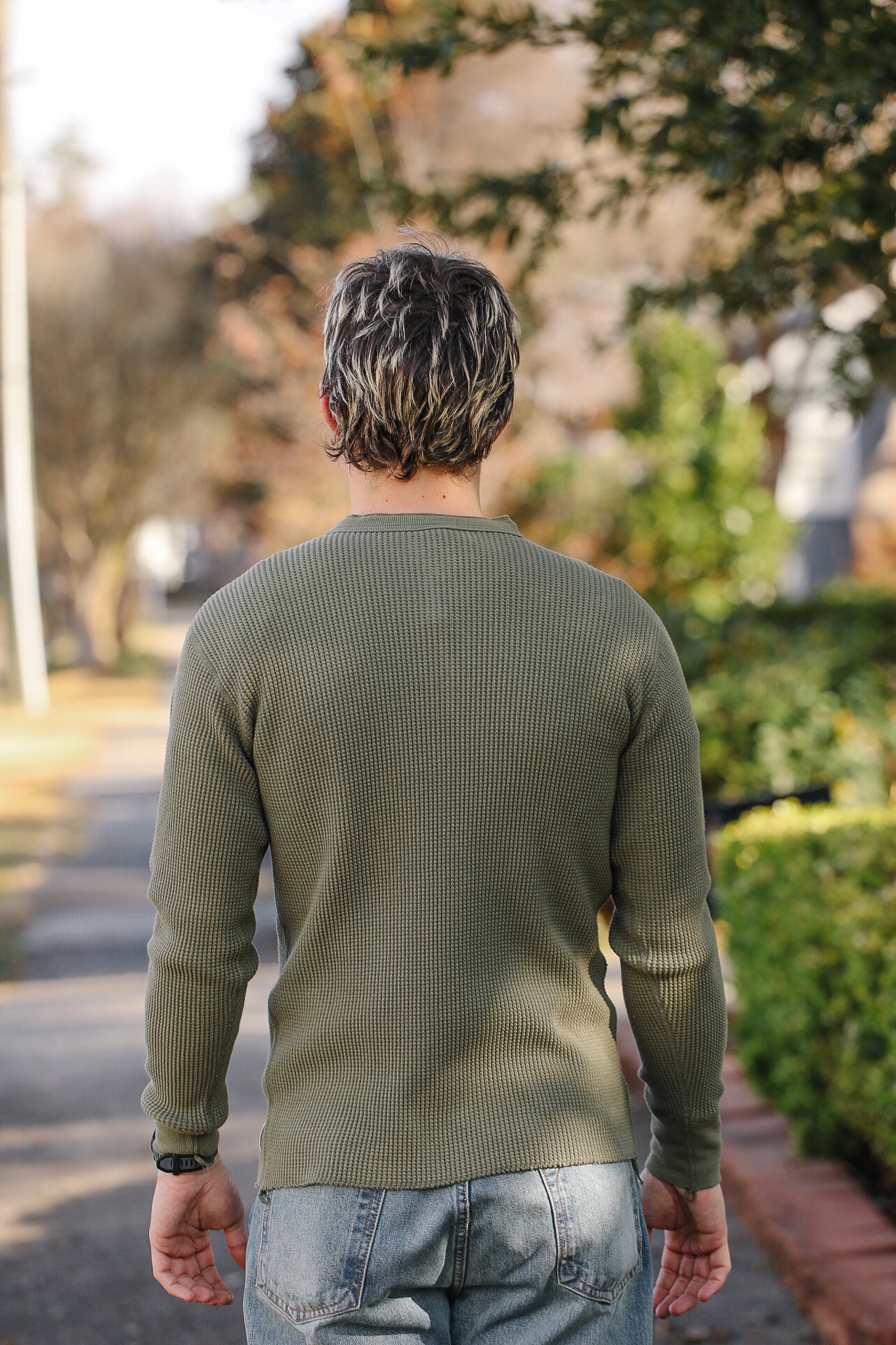 Person wearing a green sweater walking on a path with trees and bushes in the background