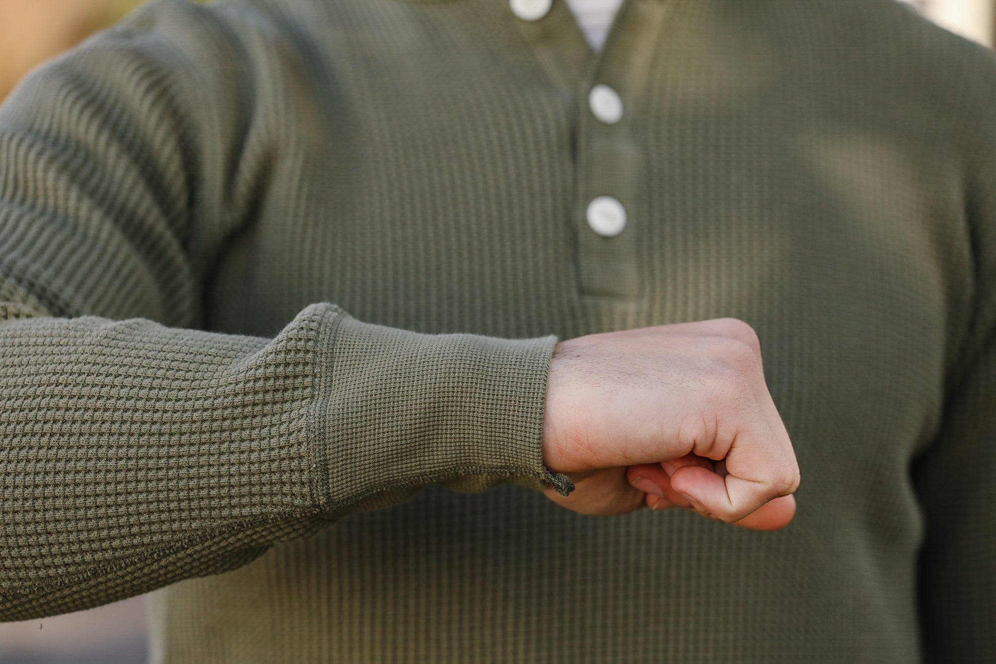 Person wearing a green textured sweater with a close-up of their fist.