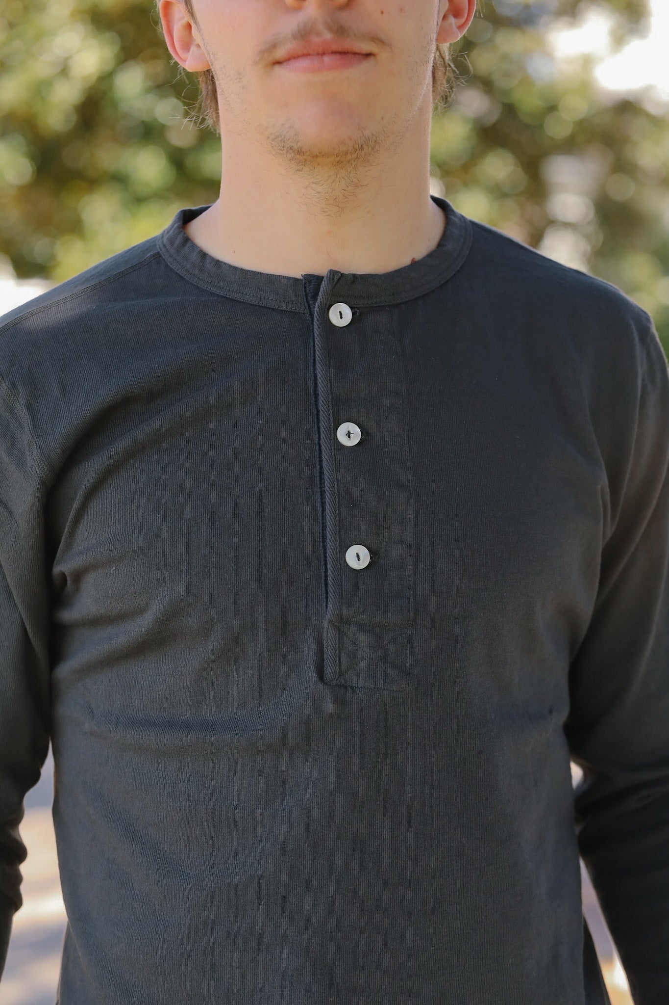 Person wearing a dark gray long-sleeve shirt with buttons against a blurred outdoor background