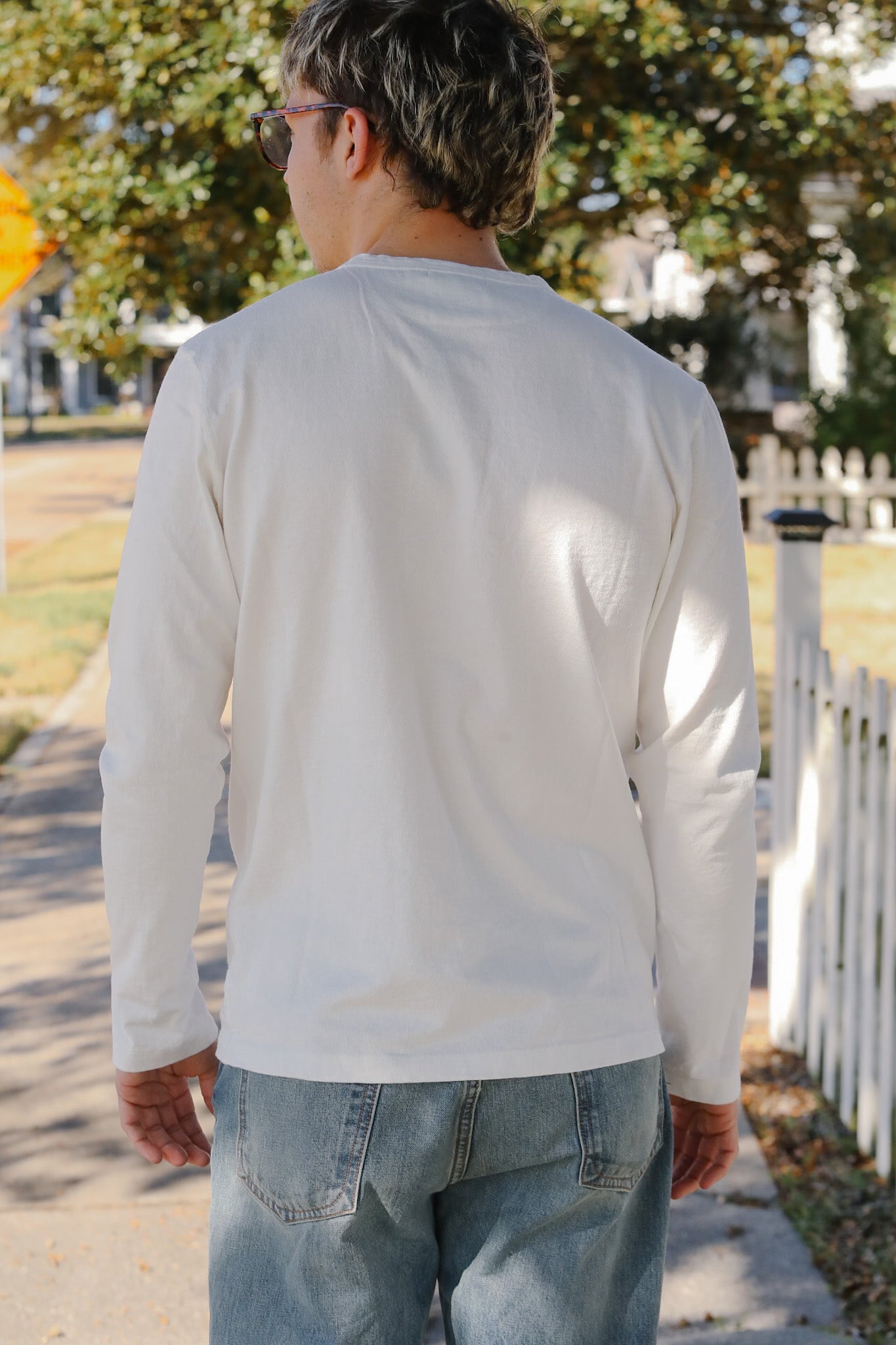 Person wearing a light gray long-sleeve shirt and blue jeans walking outdoors.
