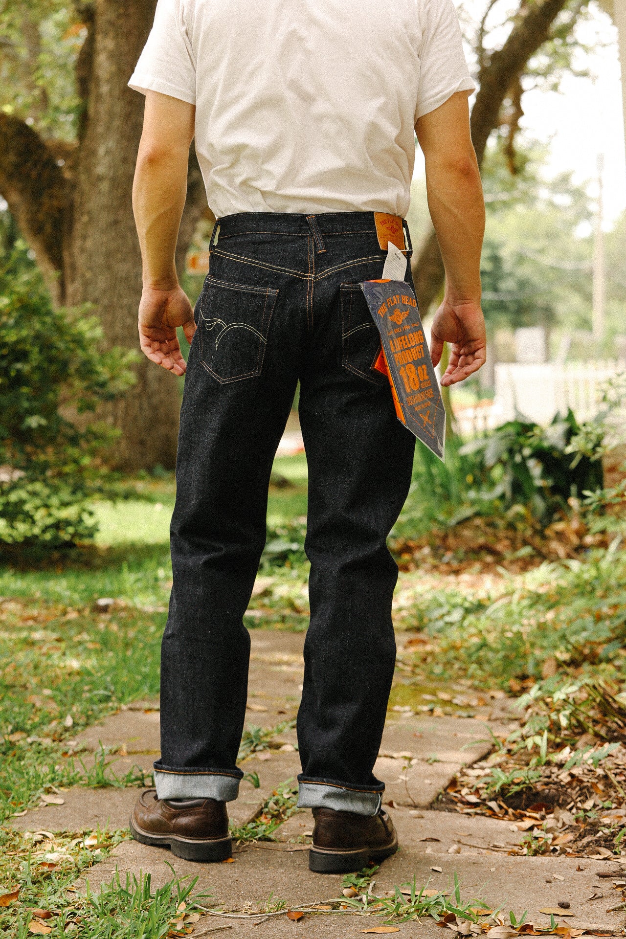 Rear view of person wearing dark indigo 18oz wide taper jeans with rolled cuffs and brown boots outdoors