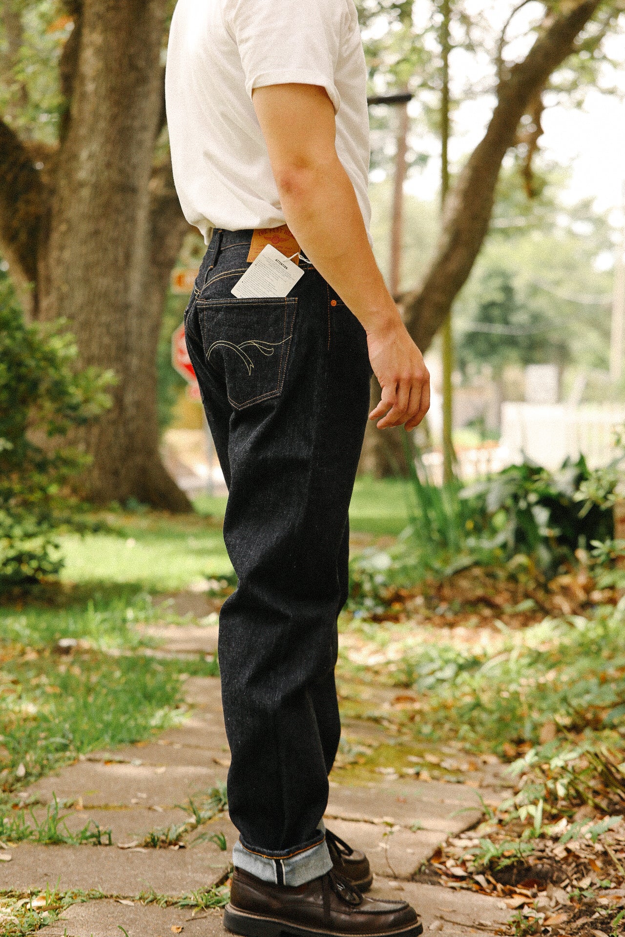 Person wearing 18oz indigo wide taper jeans outdoors on a stone pathway with white shirt and brown shoes