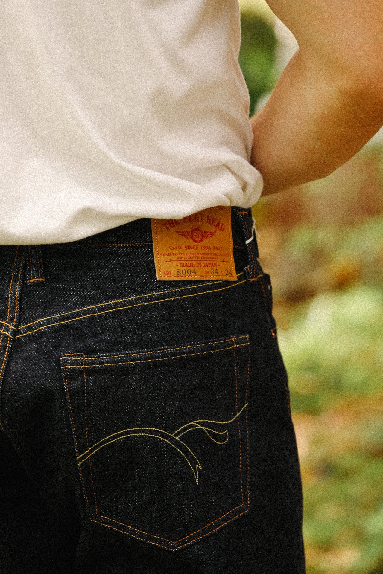 Close-up of person wearing indigo 18oz wide taper jeans by The Flat Head with leather brand patch