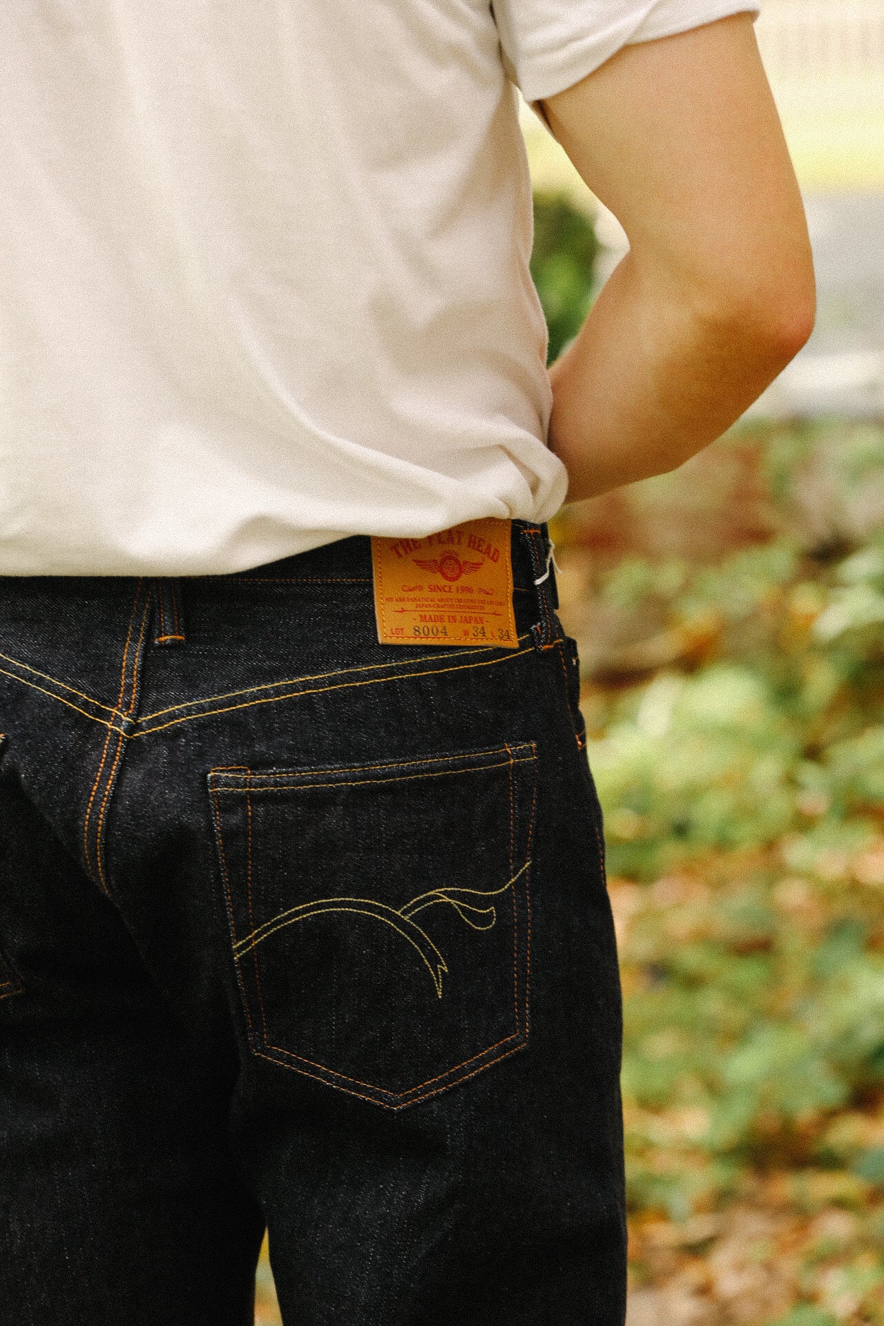 Close-up of person wearing dark indigo wide taper jeans with orange stitching and leather patch, outdoors