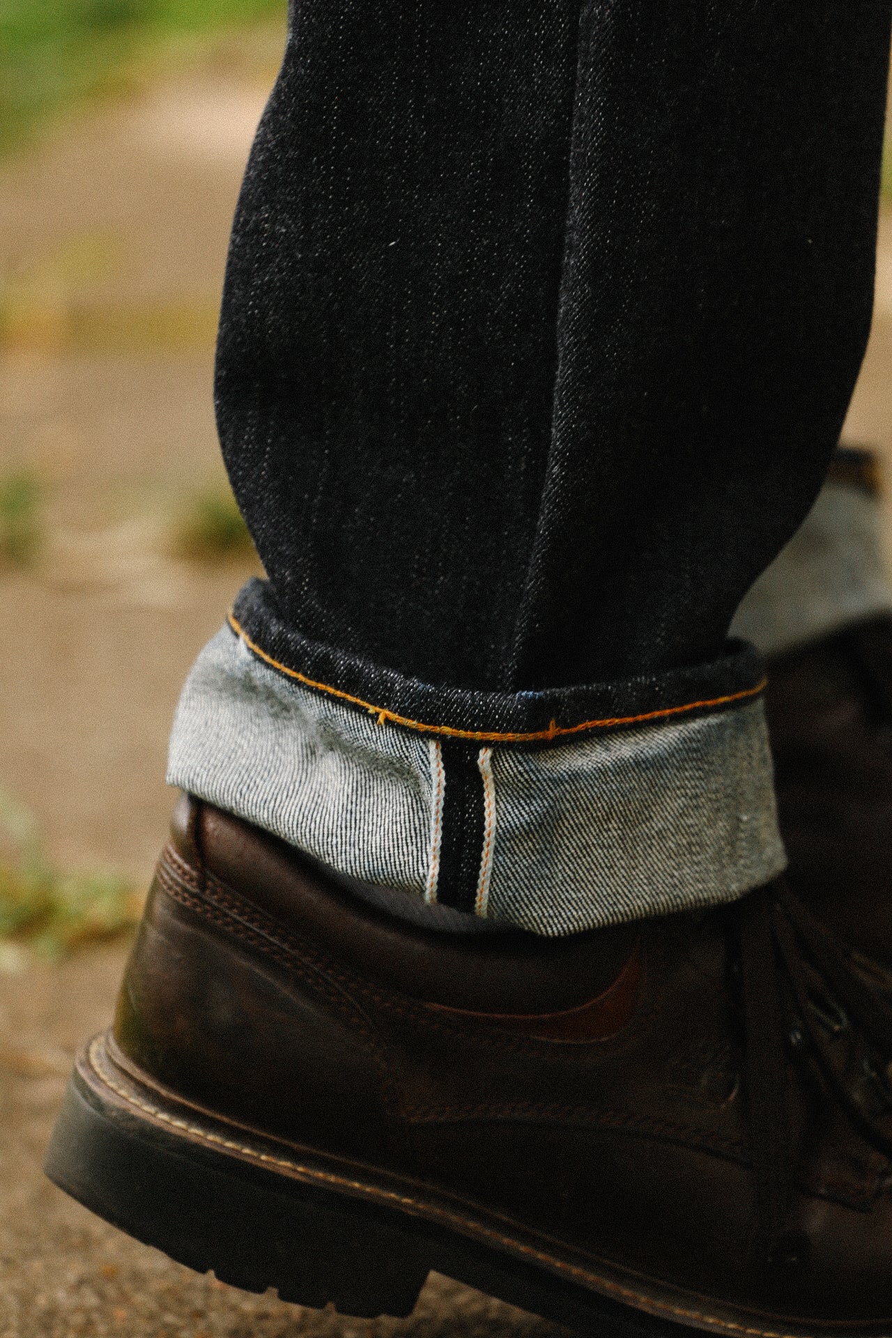 Cuffed indigo 18oz wide taper jeans paired with brown leather boots on outdoor pavement