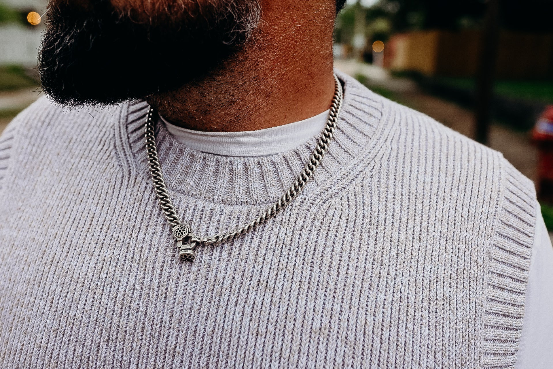 Man wearing a silver chain necklace with pendant, gray knit sweater over white shirt