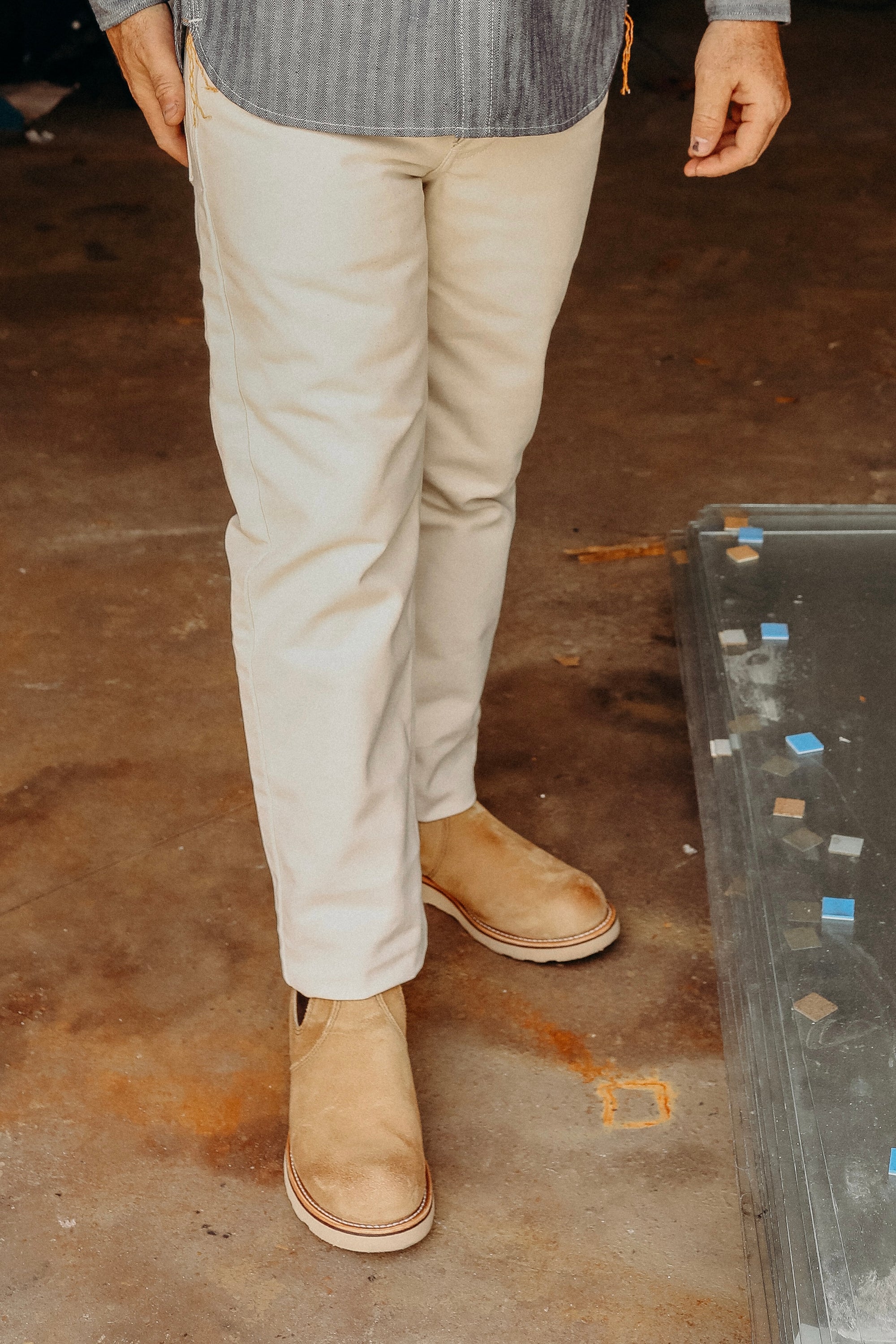 Person wearing beige pants and tan leather work boots standing on a concrete floor near glass panels