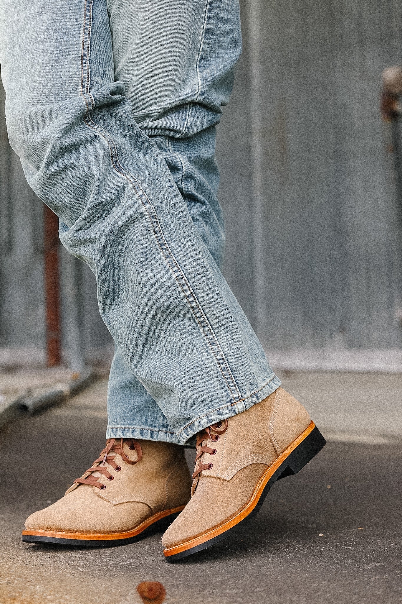 Tan leather shoes with black soles worn with light blue jeans on a concrete surface.