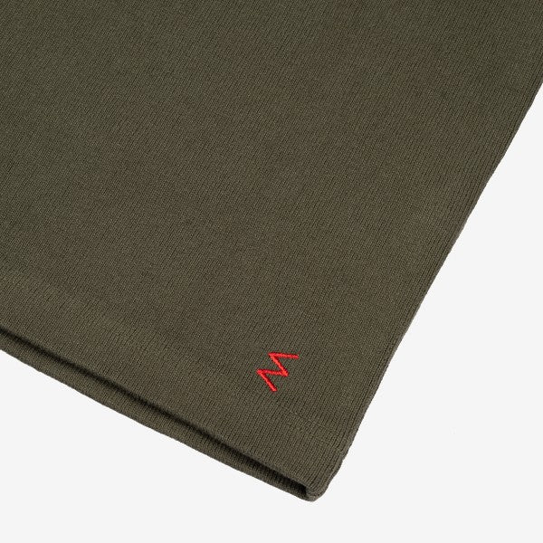 Close-up of an olive green textile fabric with a small red embroidered 'W' detail on Iron Shop Provisions garment