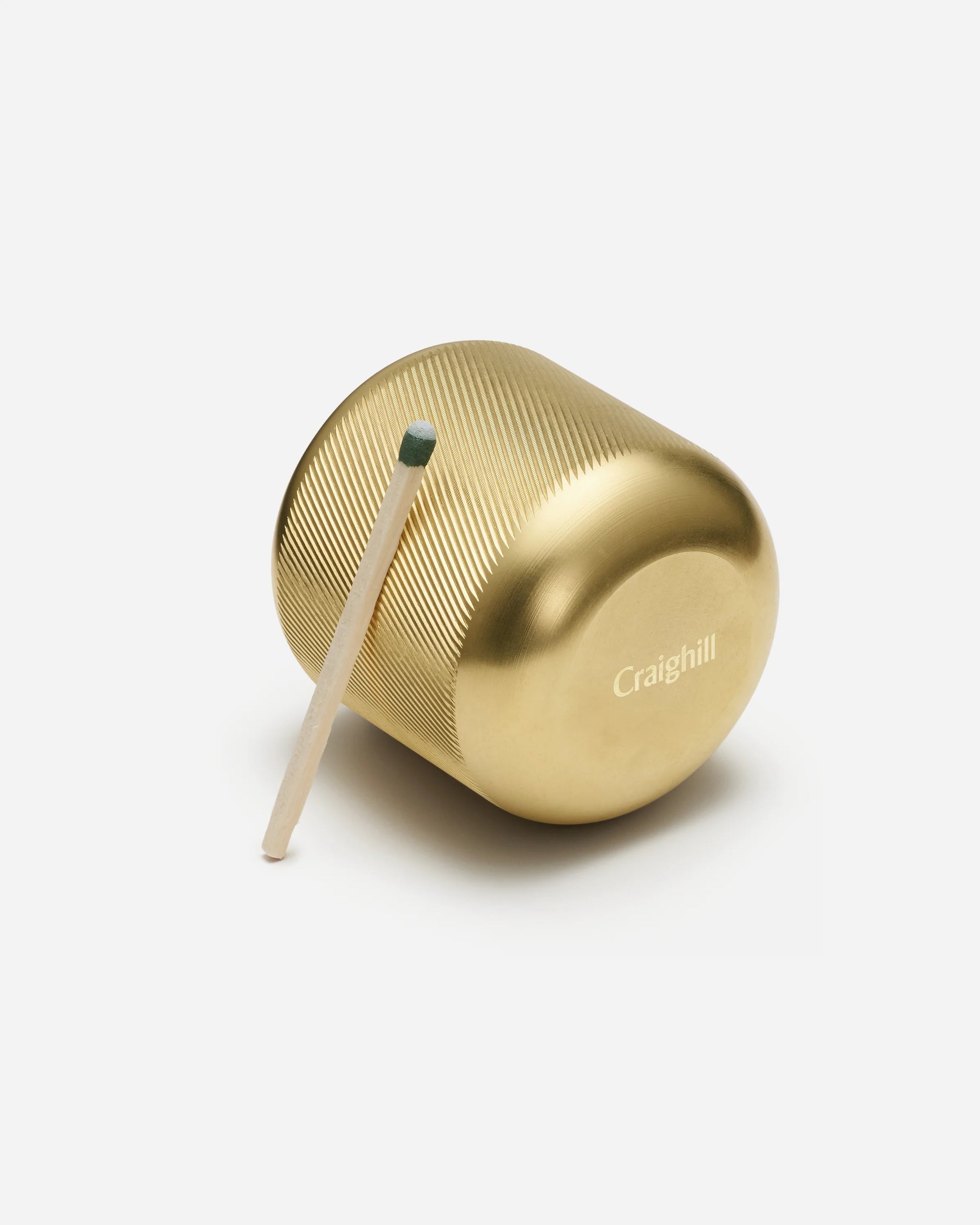 Gold-tone Craighill brass candle snuffer with textured grip and matchstick on white background