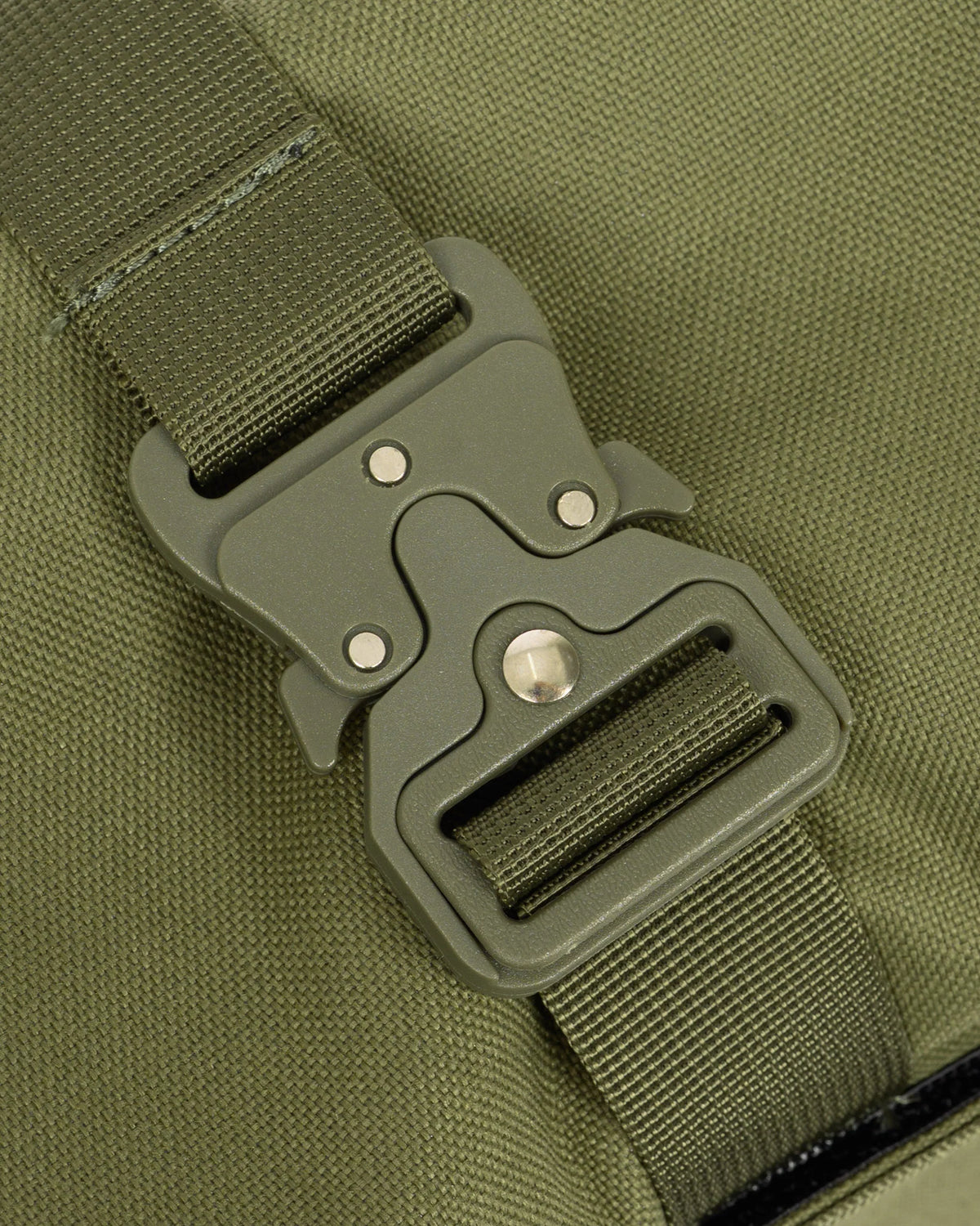 Close-up of an olive green nylon webbing strap with a matching dark gray plastic quick-release buckle on a bag.