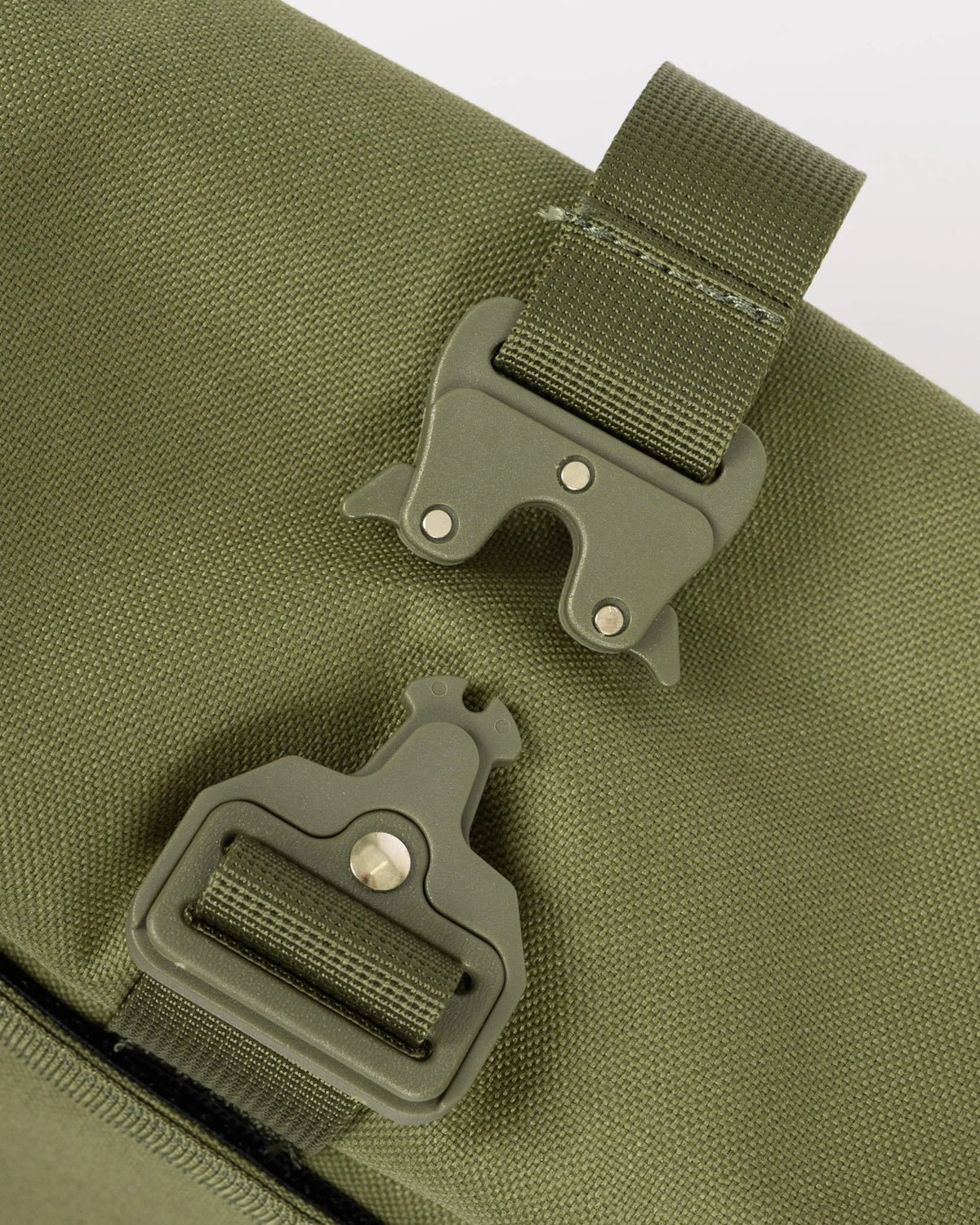 Close-up of an olive green canvas bag with two matching plastic buckle straps on a light gray background.