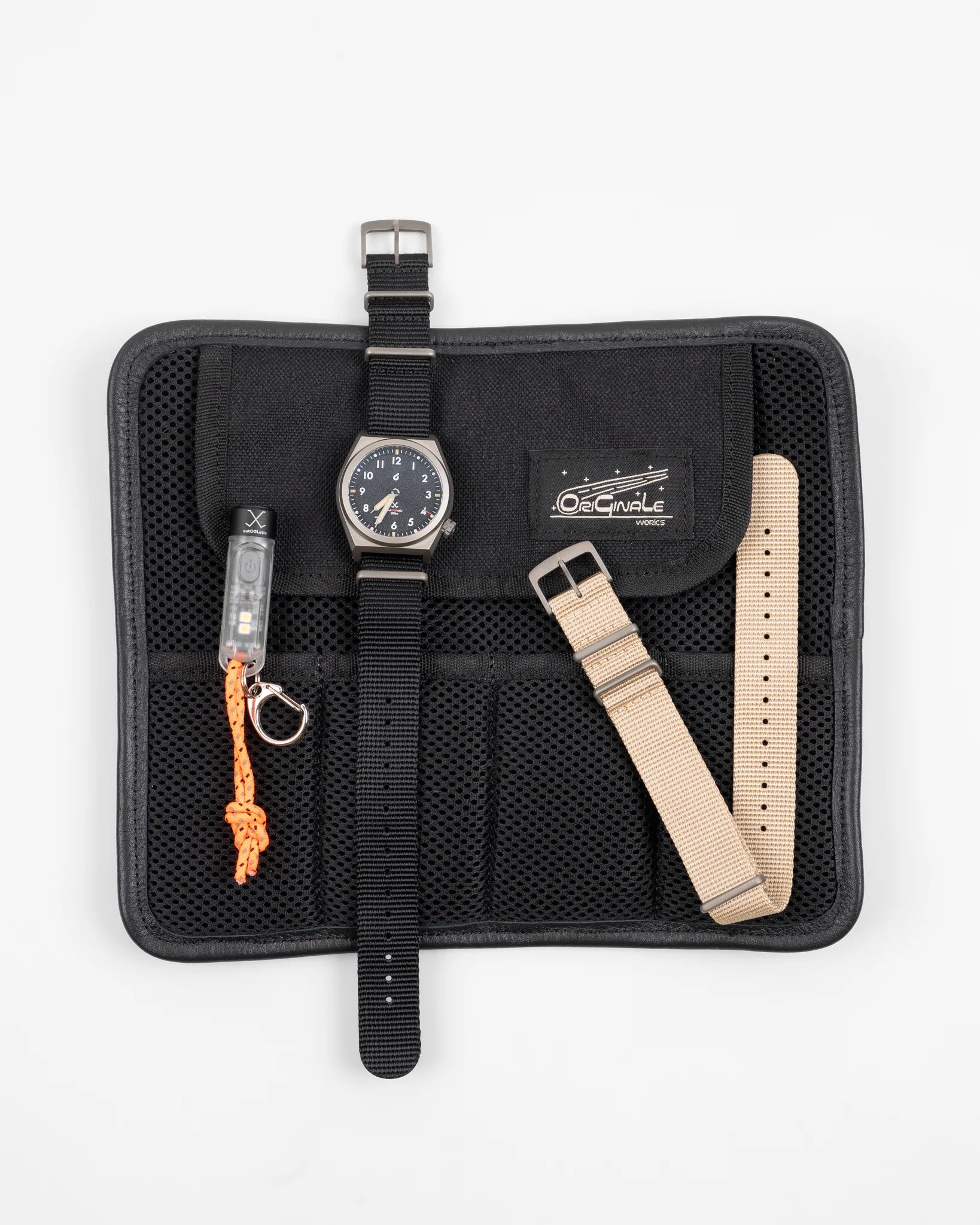 Autoglatic field watch with black nylon strap on black mesh storage roll with beige extra strap and small LED keychain