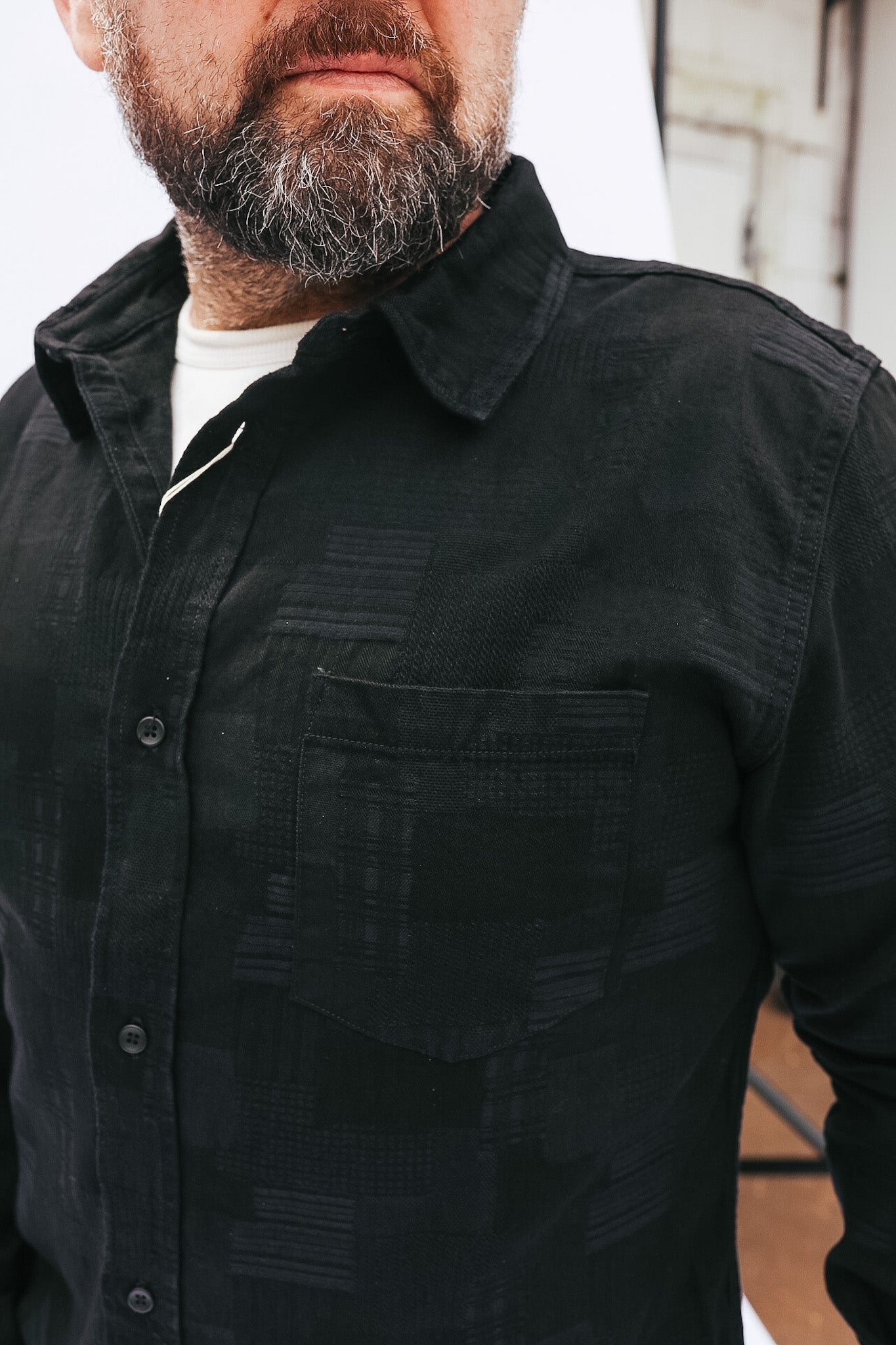 Man wearing a black shirt with a textured pattern, standing against a neutral background.