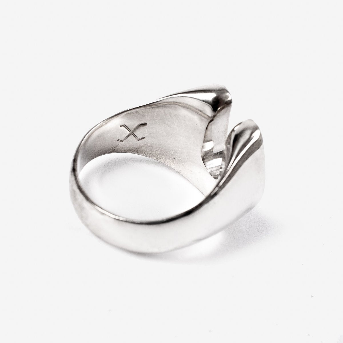 Close-up of a polished silver ring with a rustic design and an engraved X inside, on white background