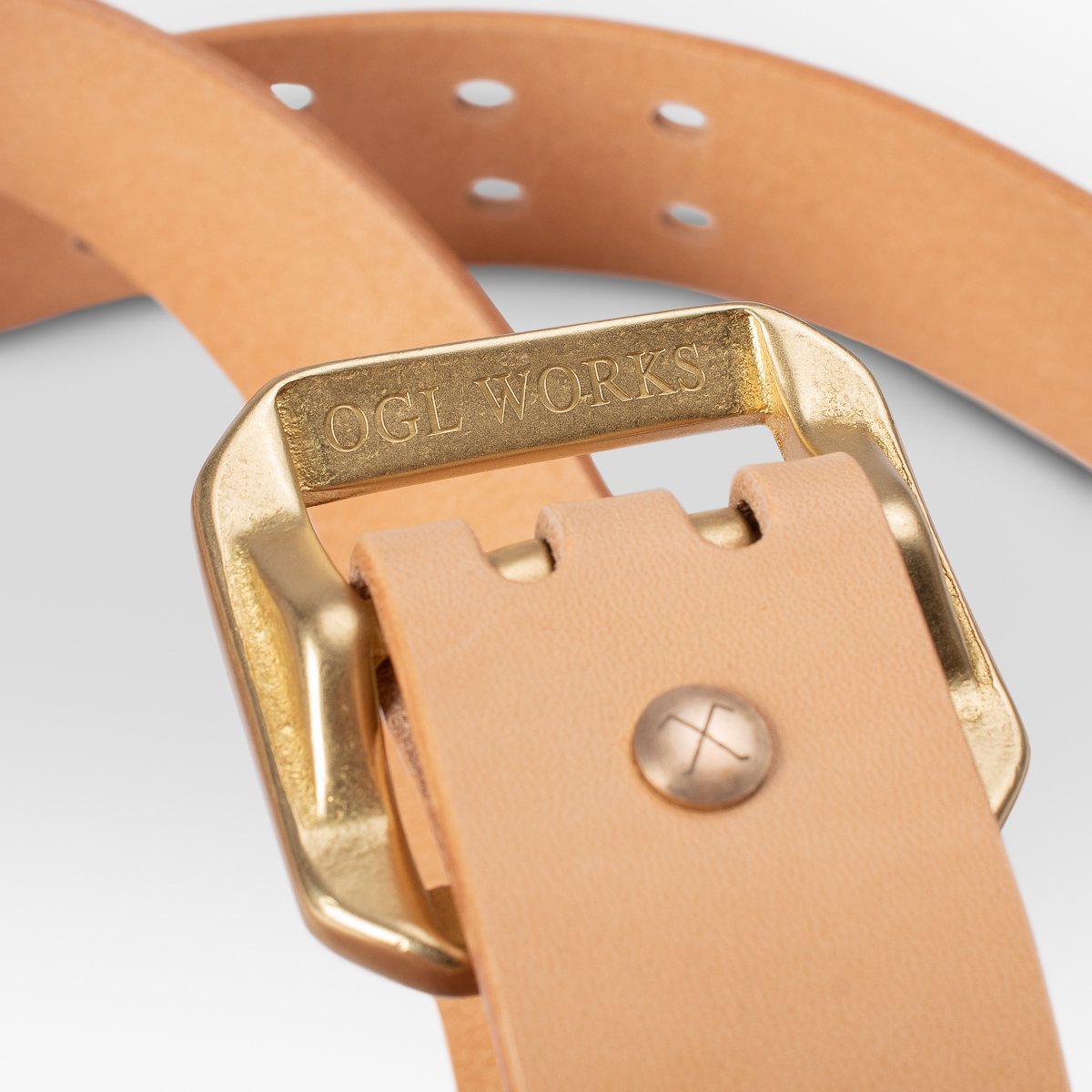 Close-up of natural leather belt with gold OGL WORKS buckle and brass rivet detail