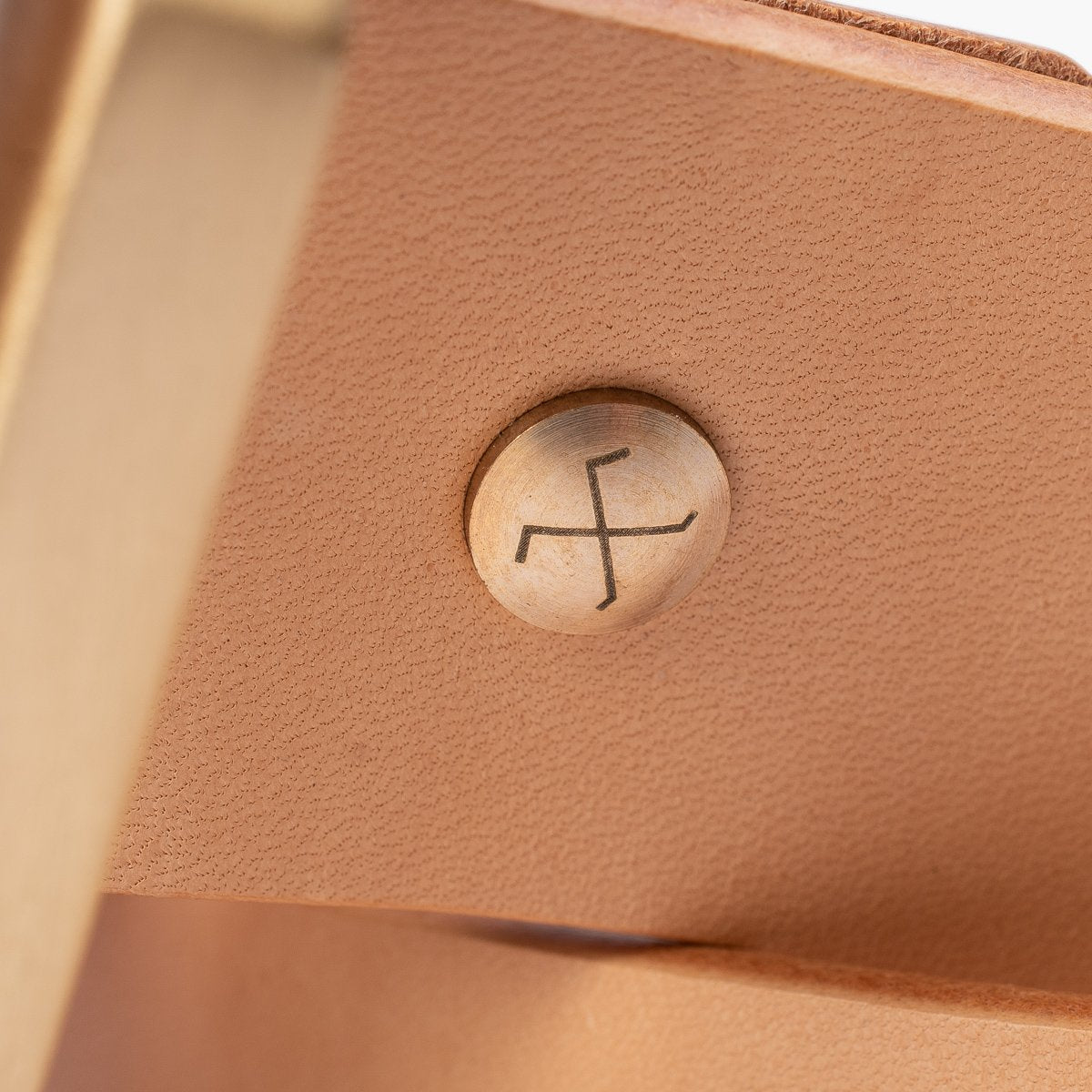 Close-up of a leather piece secured with a brass rivet stamped with Iron Shop Provisions logo