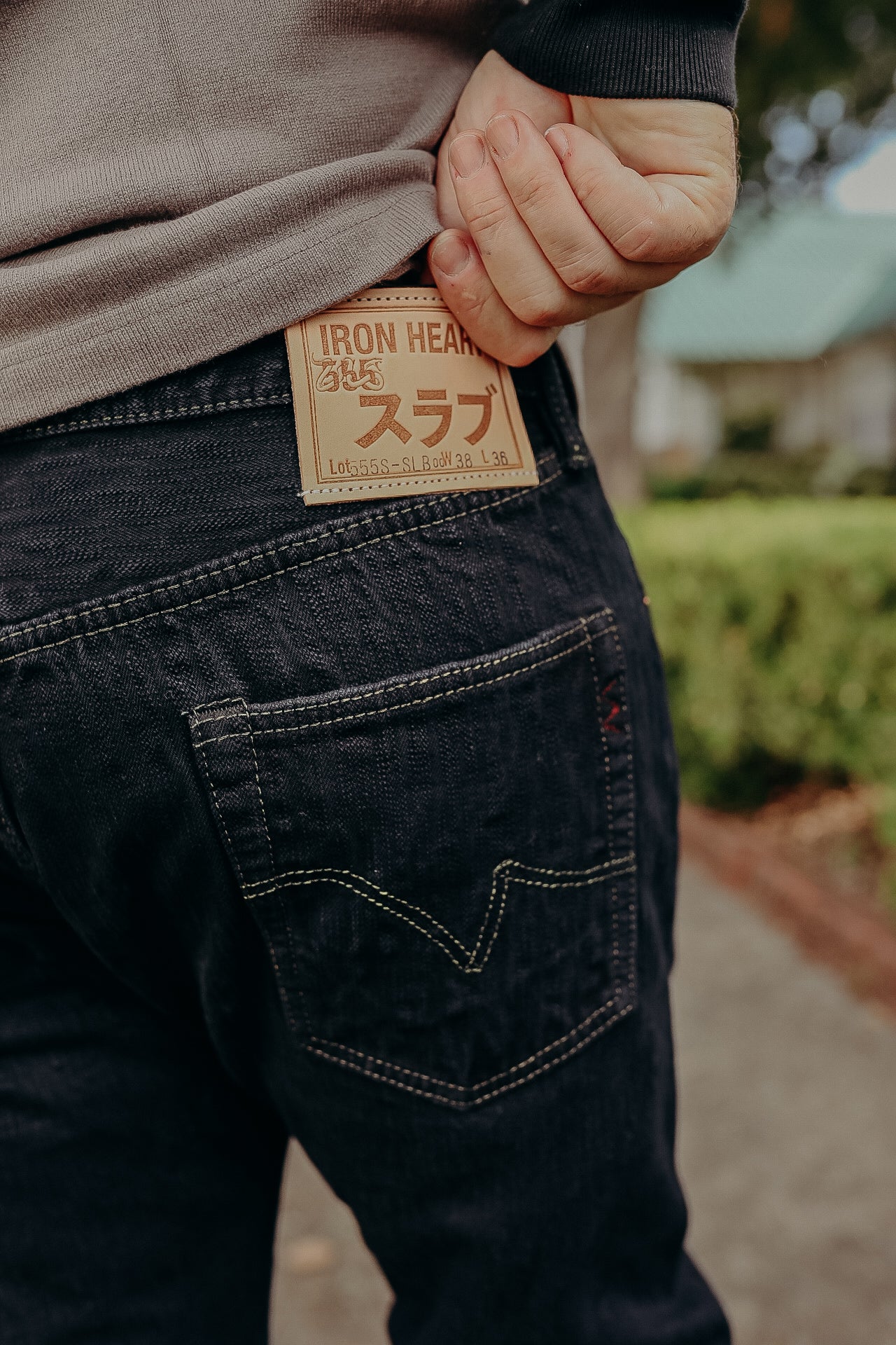Close-up of person wearing Iron Heart dark denim jeans with leather brand patch on back pocket outdoors