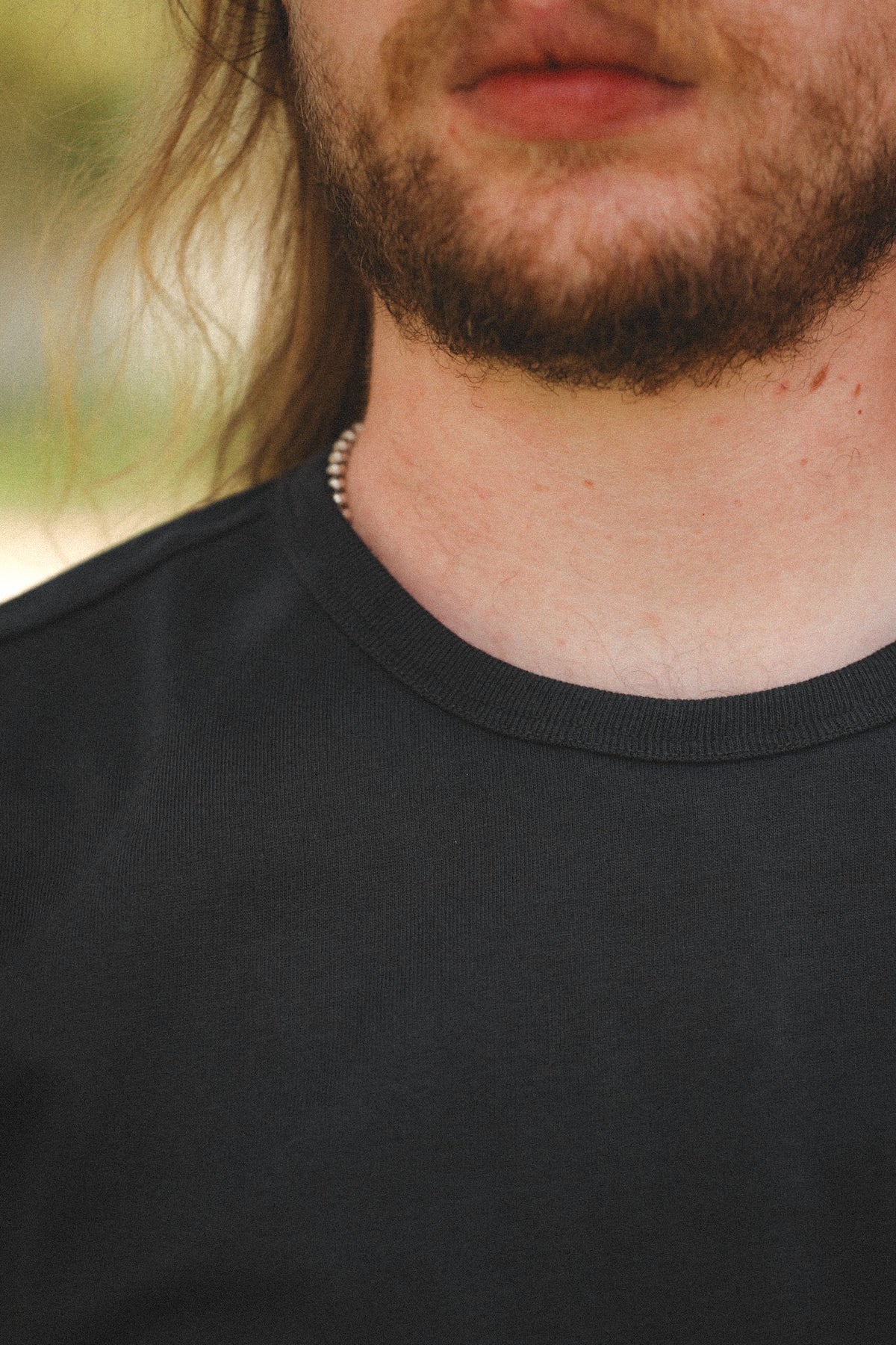 Close-up of a man wearing a black crew-neck t-shirt, showing his chin, beard, neck, and the collar of the shirt.