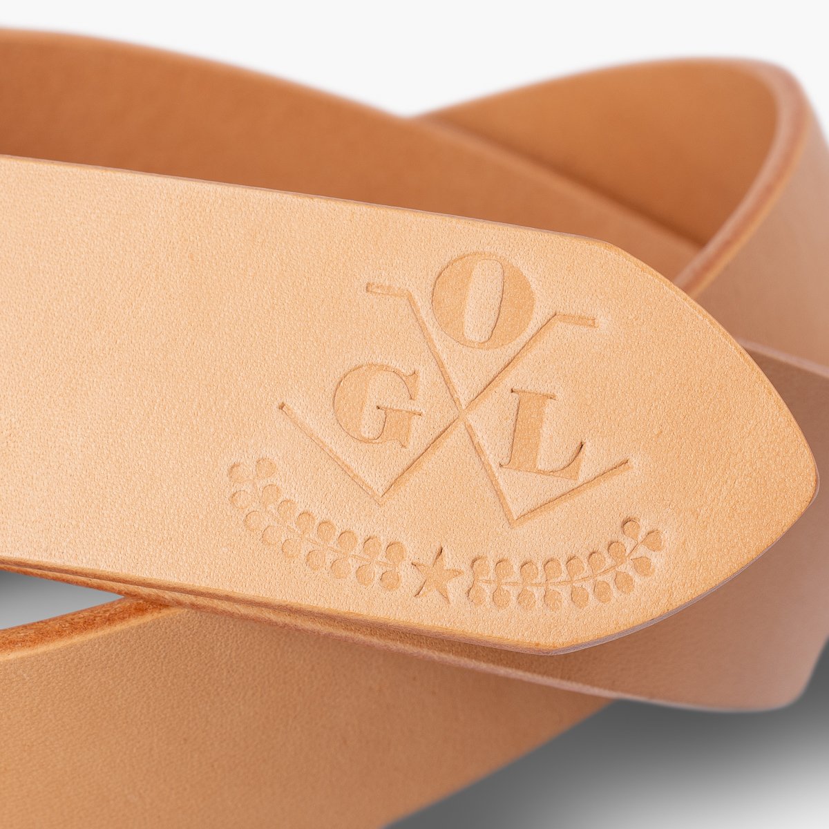 Close-up of natural leather belt with embossed OGL logo and decorative star and leaves detail