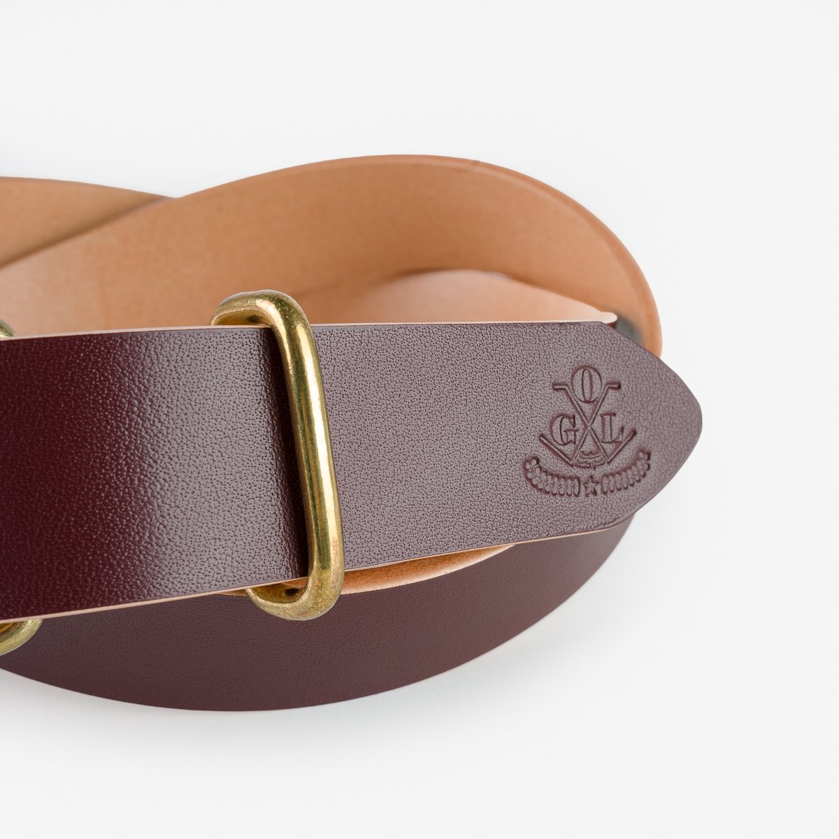 Close-up of burgundy leather belt with brass buckle and embossed logo on white background