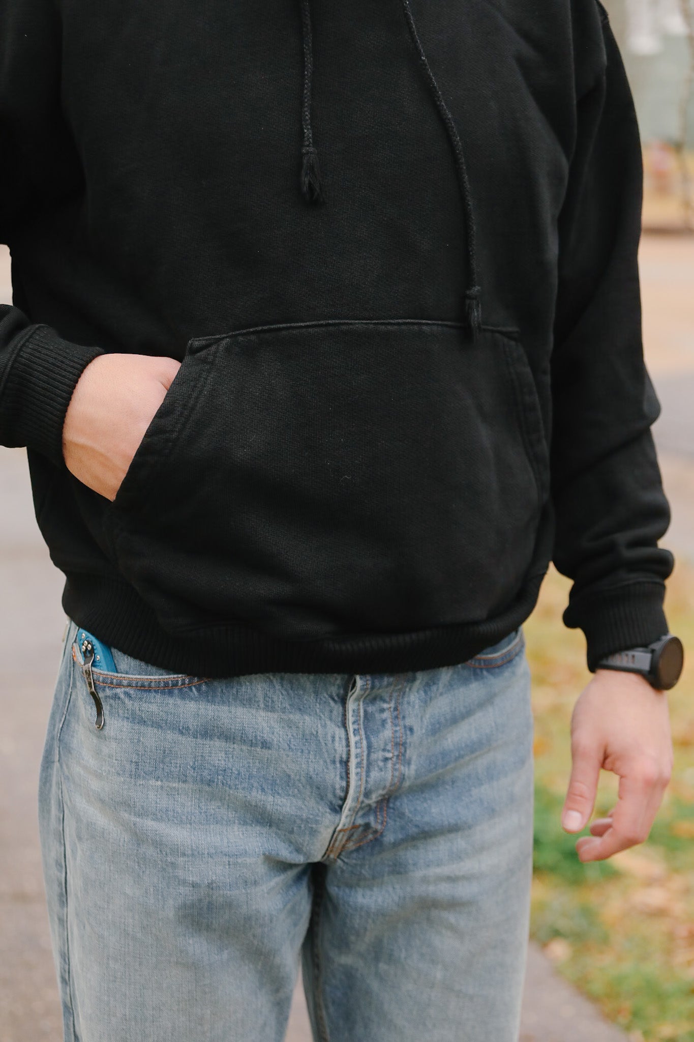 Person wearing a black hoodie and light blue jeans with a blurred outdoor background