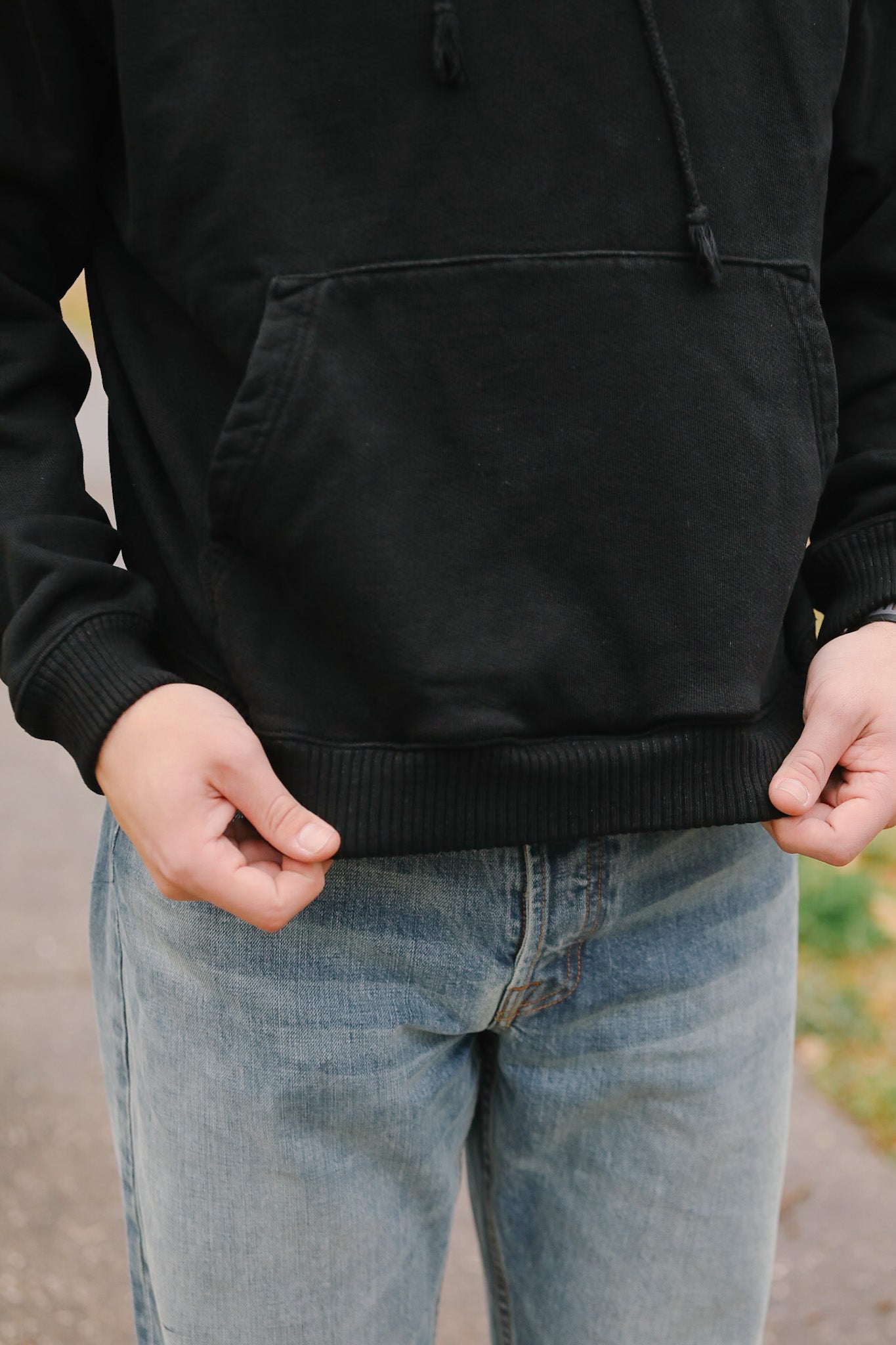 Person wearing a black hoodie and light blue jeans with a blurred background