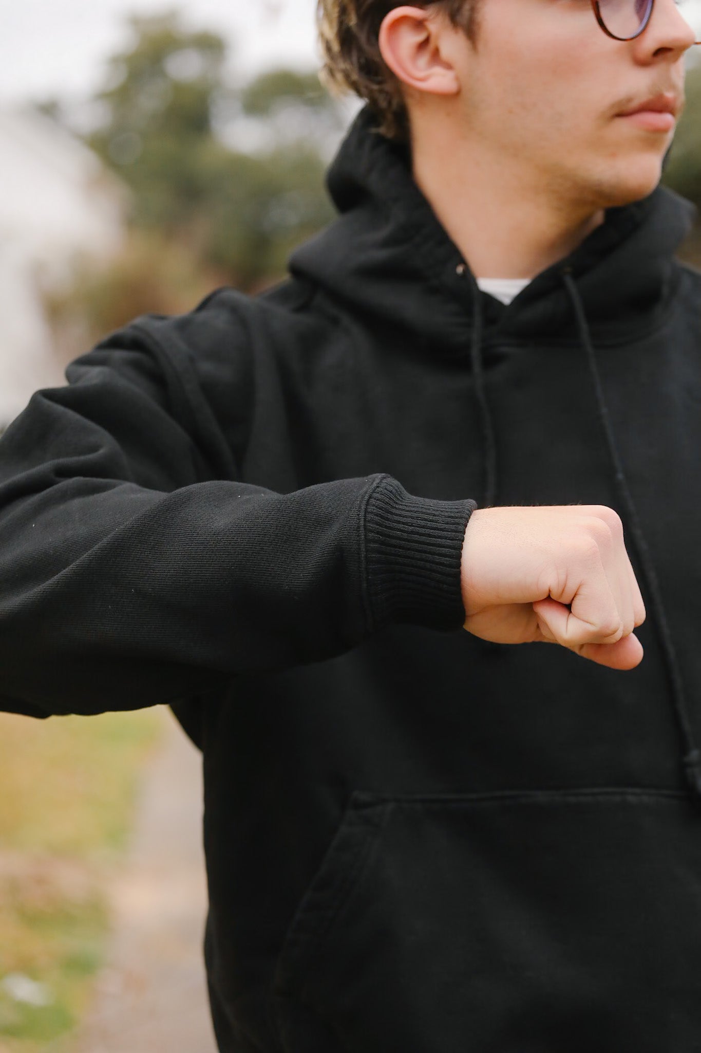 Person wearing a black hoodie outdoors with a blurred background