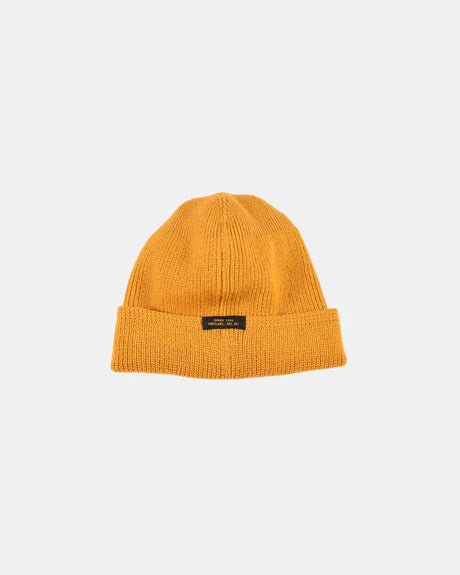 Old gold wool knit watch cap with leather patch label laid flat on white background