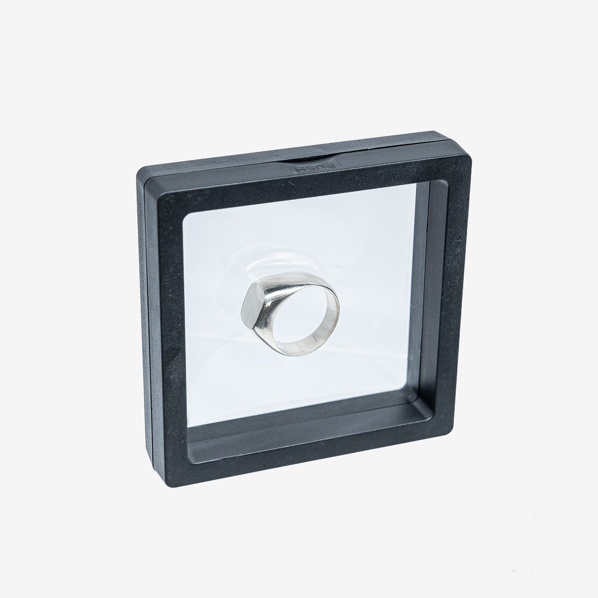 Silver metal signet ring displayed in a black frame case with transparent cover on white background