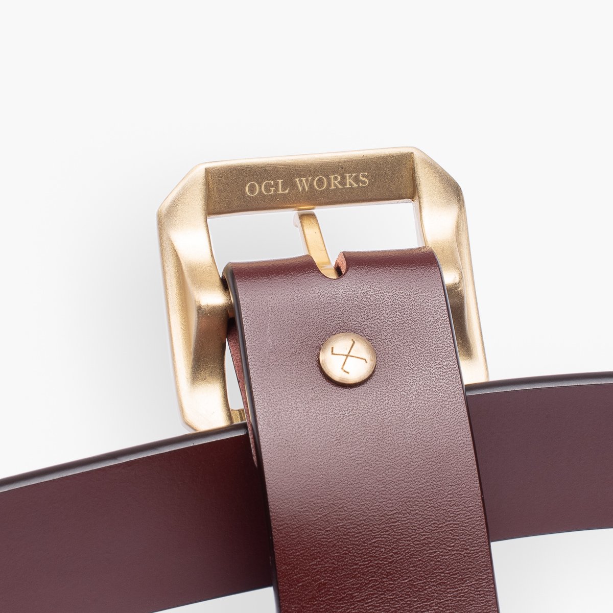 Close-up of brown leather belt with brass buckle engraved OGL WORKS and brass rivet detail