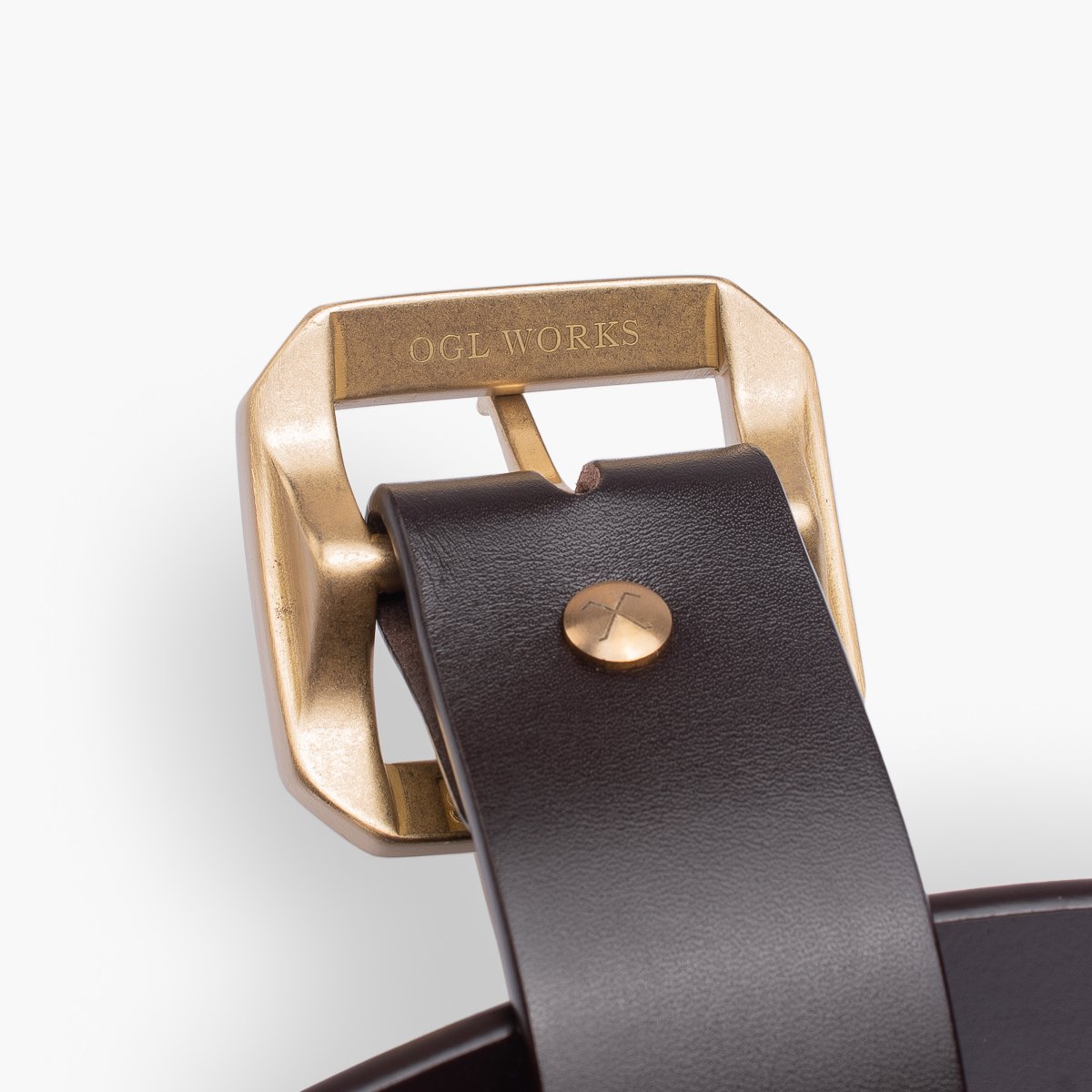 Close-up of dark brown leather belt with brass buckle engraved OGL WORKS and brass rivet