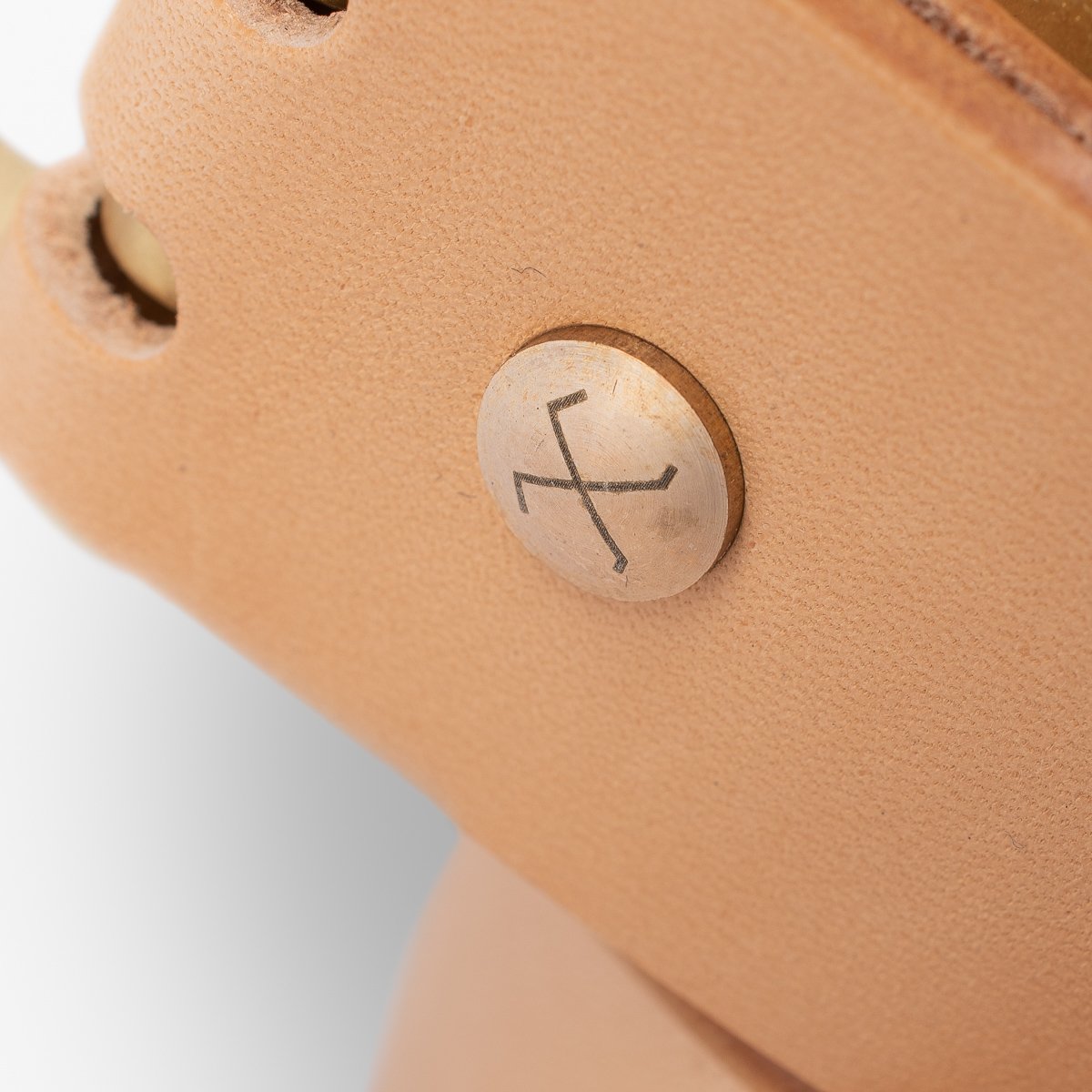Close-up of tan leather strap with metal rivet engraved with crossed tools logo at Iron Shop Provisions