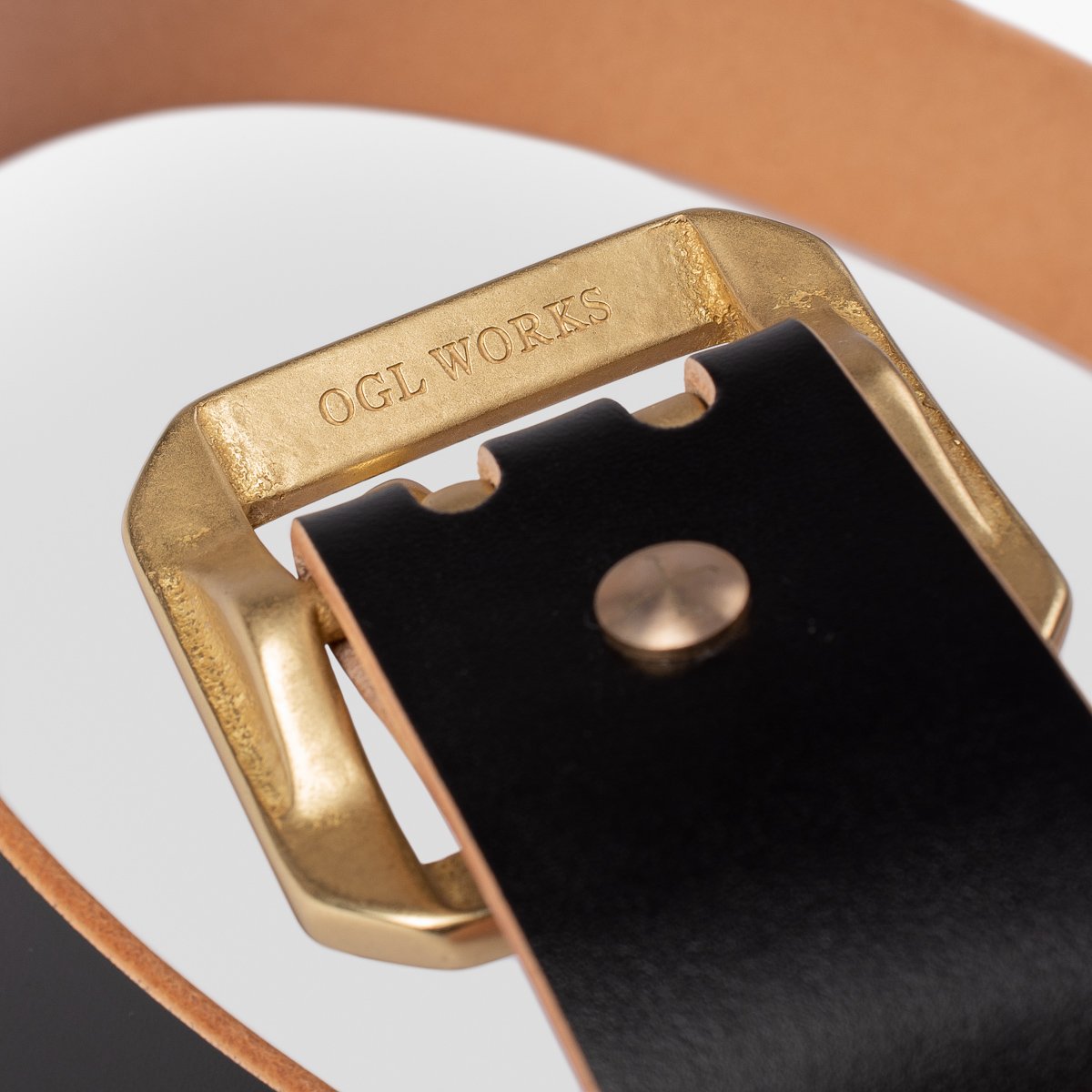 Close-up of brass belt buckle engraved with OGL WORKS on black leather belt