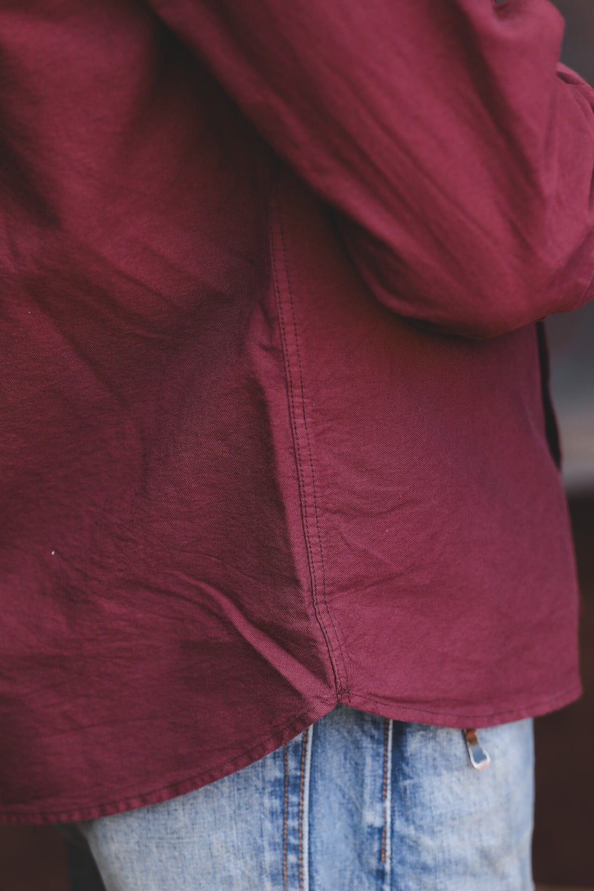 A close-up shot of a person wearing a textured, deep burgundy long-sleeve shirt tucked into light-wash blue jeans.