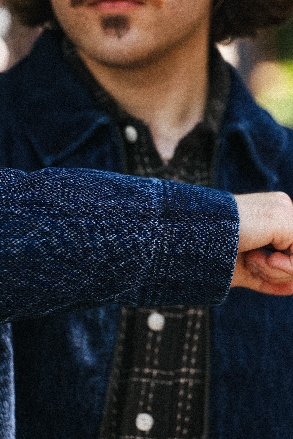 Close-up of a person wearing a dark blue textured corduroy jacket over a black patterned shirt, with the person's hand pointing toward the sleeve.