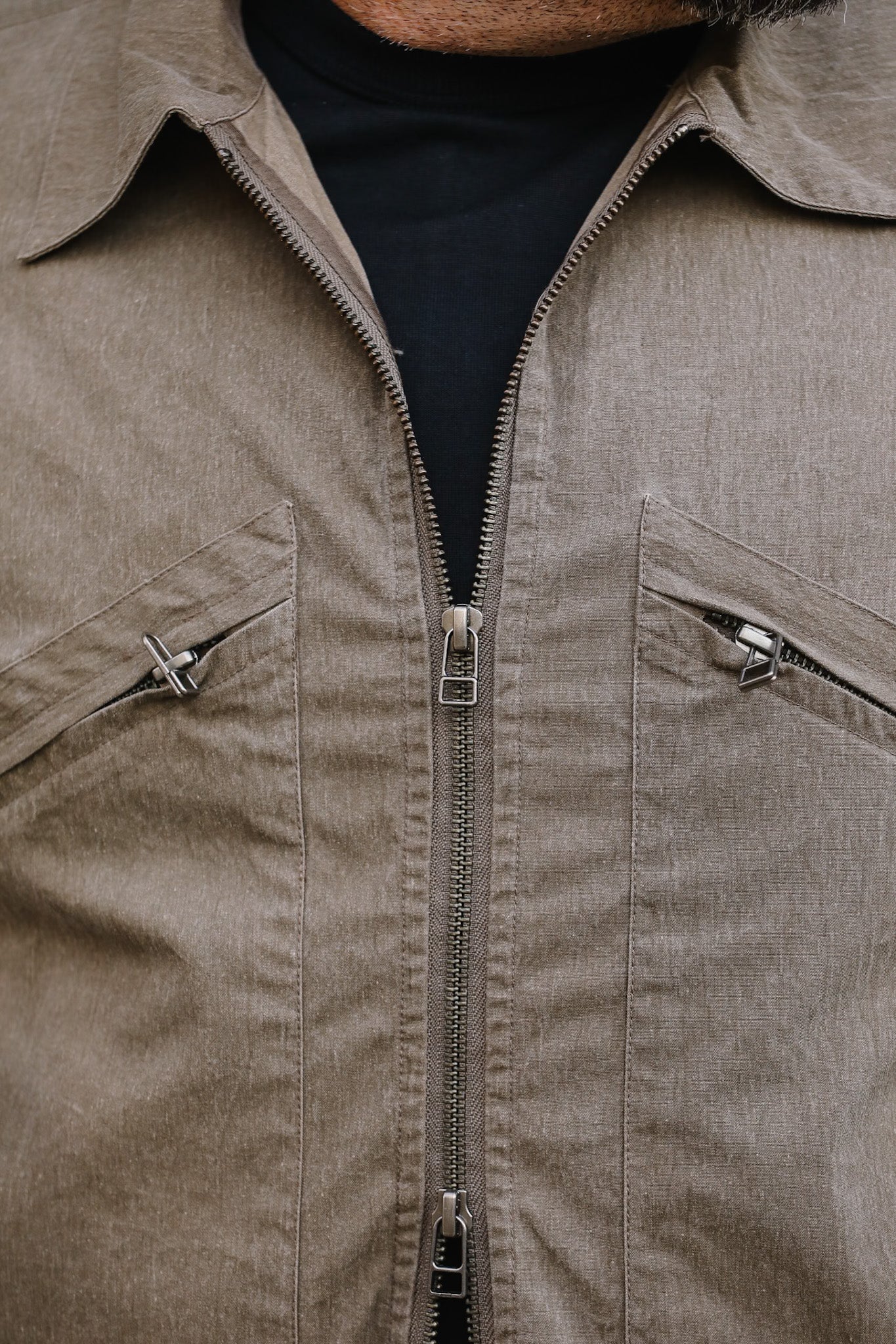 Close-up of a beige jacket with zippers and a black shirt underneath.