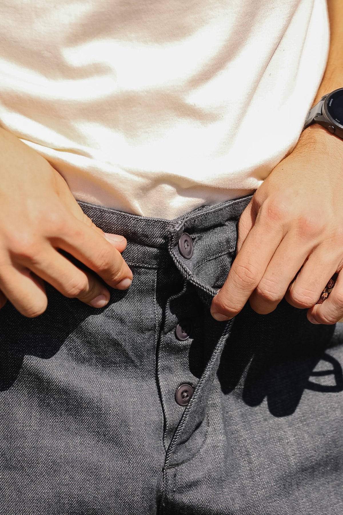 Close-up of a person wearing dark gray denim jeans and a cream-colored t-shirt, adjusting the waistband of the jeans with both hands.